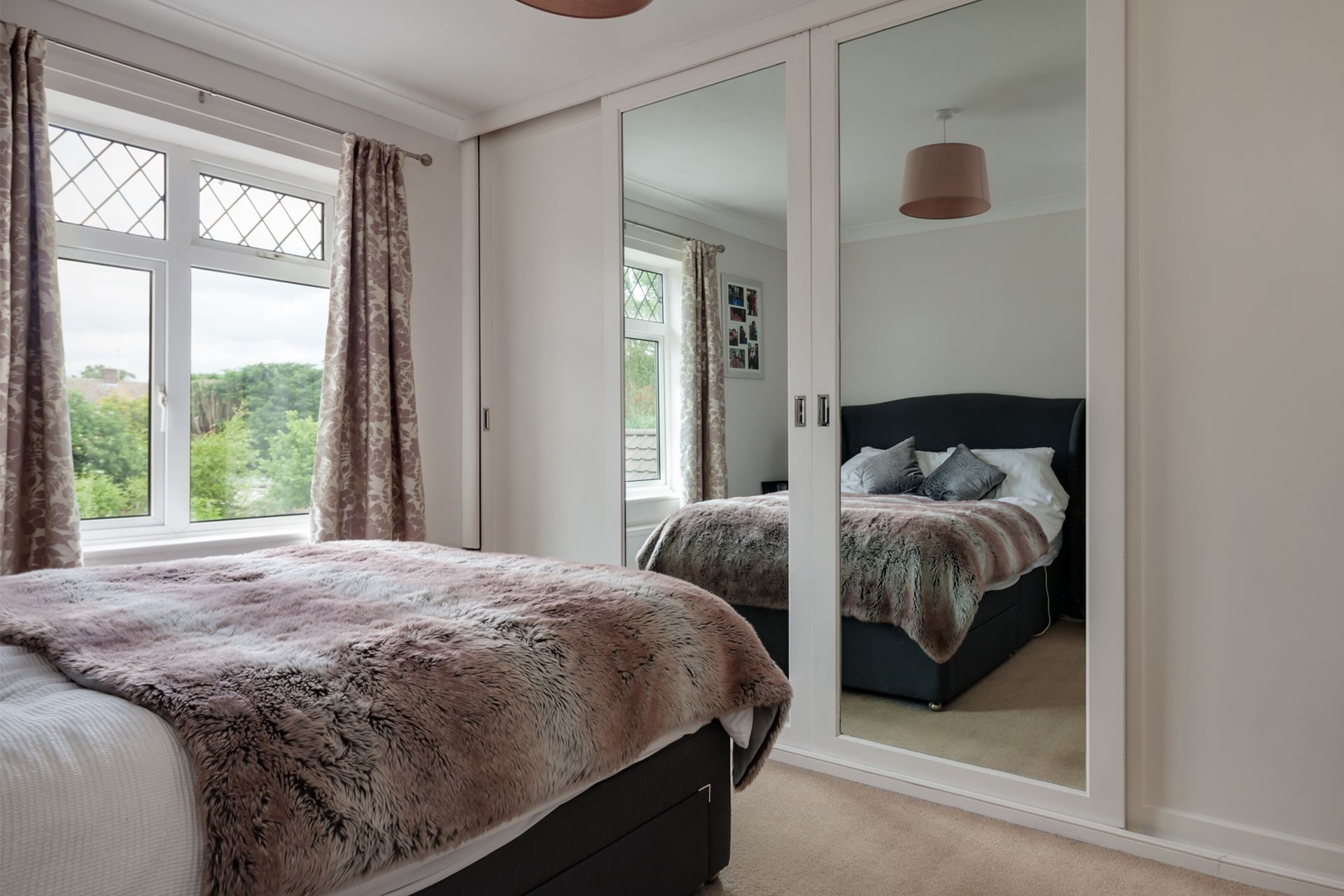 Bright bedroom with bed, mirrored wardrobe, and large windows overlooking greenery.