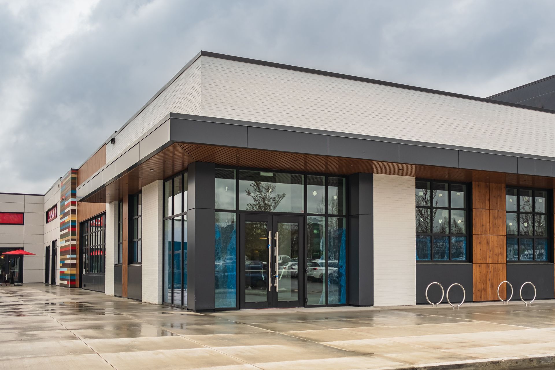 Modern storefront with large glass windows and a white-and-brown exterior on a wet sidewalk.