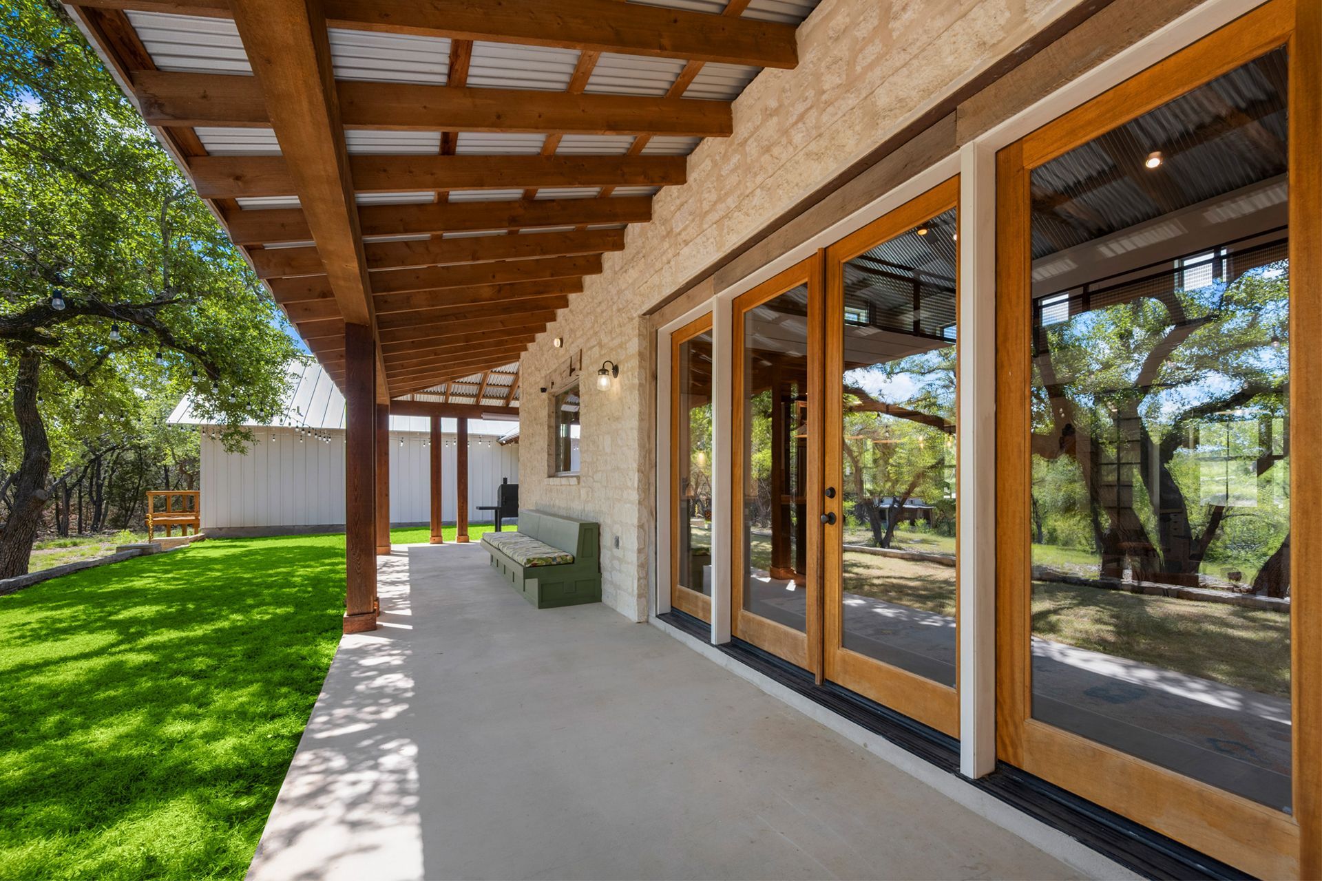 Covered patio with wood ceiling, glass doors, and green lawn beside a house.