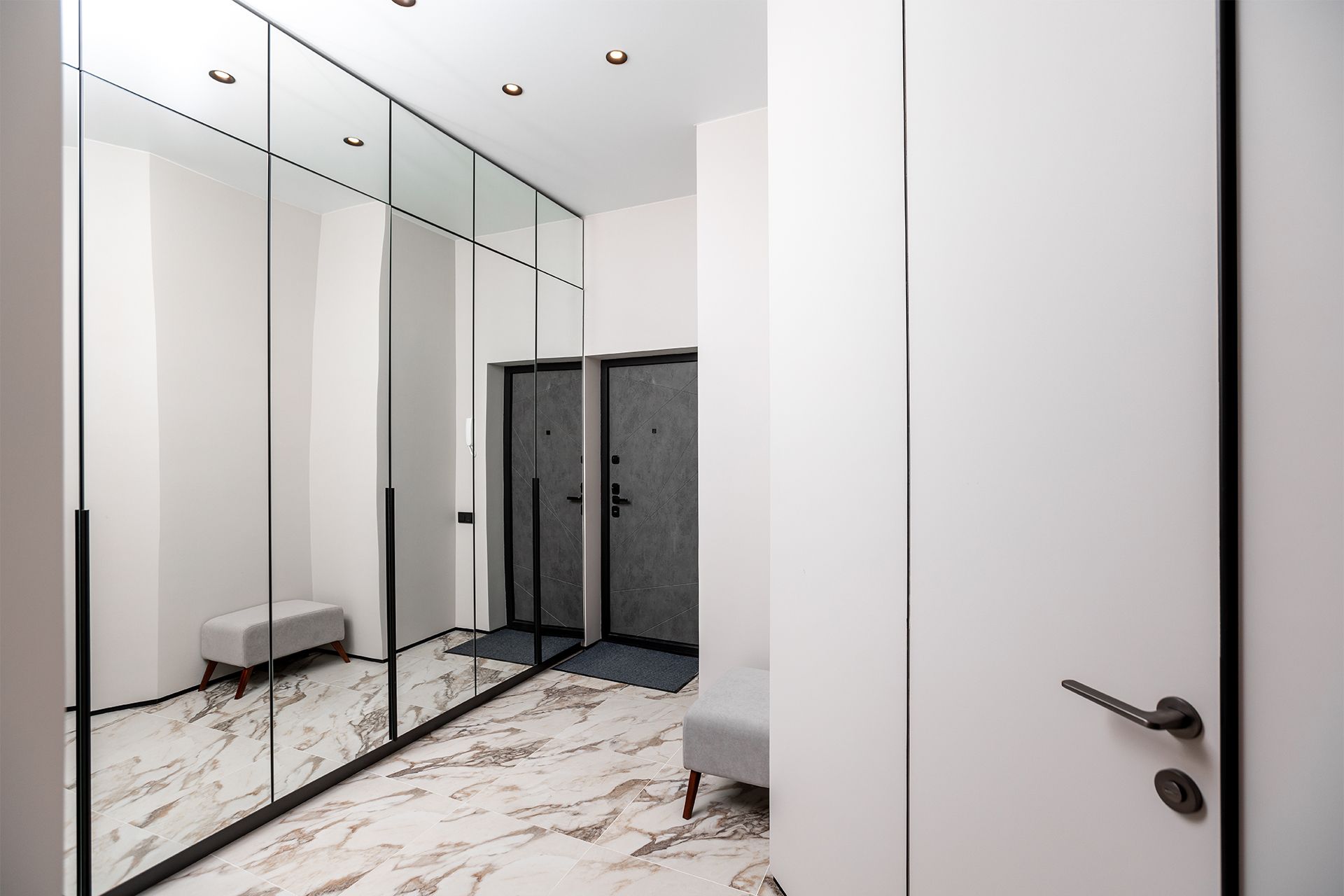 Bright modern hallway with mirrored closet doors, white walls, and marble floor.