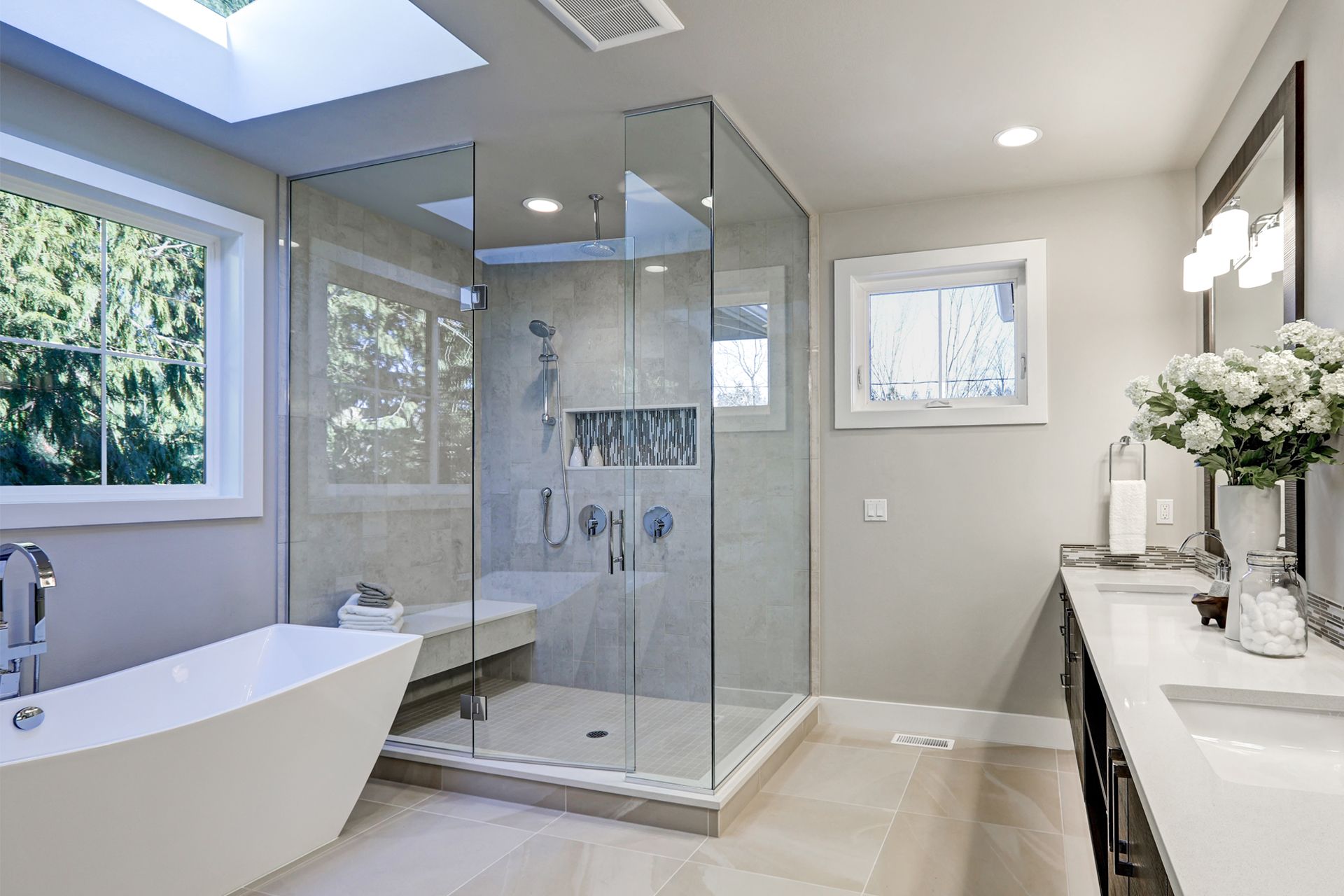 Modern bathroom with freestanding tub, glass shower, vanity, and skylight.