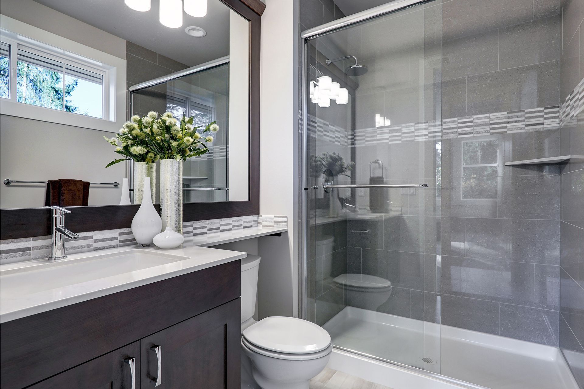Modern bathroom with dark vanity, white countertop, flowers, and a glass-enclosed bathtub/shower.
