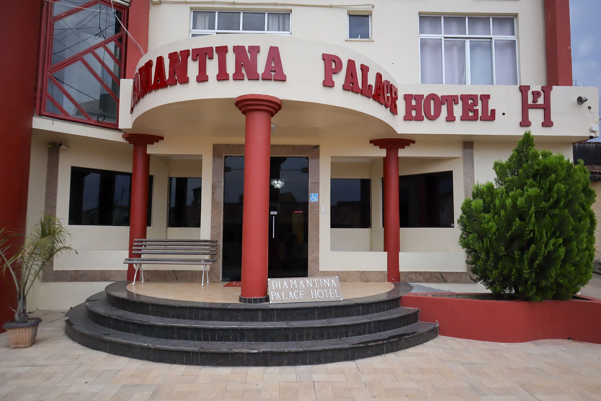 Entrada do Hotel Palmar com colunas vermelhas e placa curva acima dos degraus e banco.
