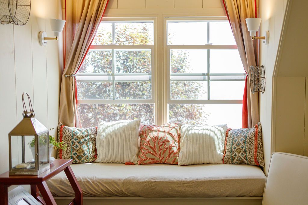 A living room with a window seat filled with pillows and a lantern.
