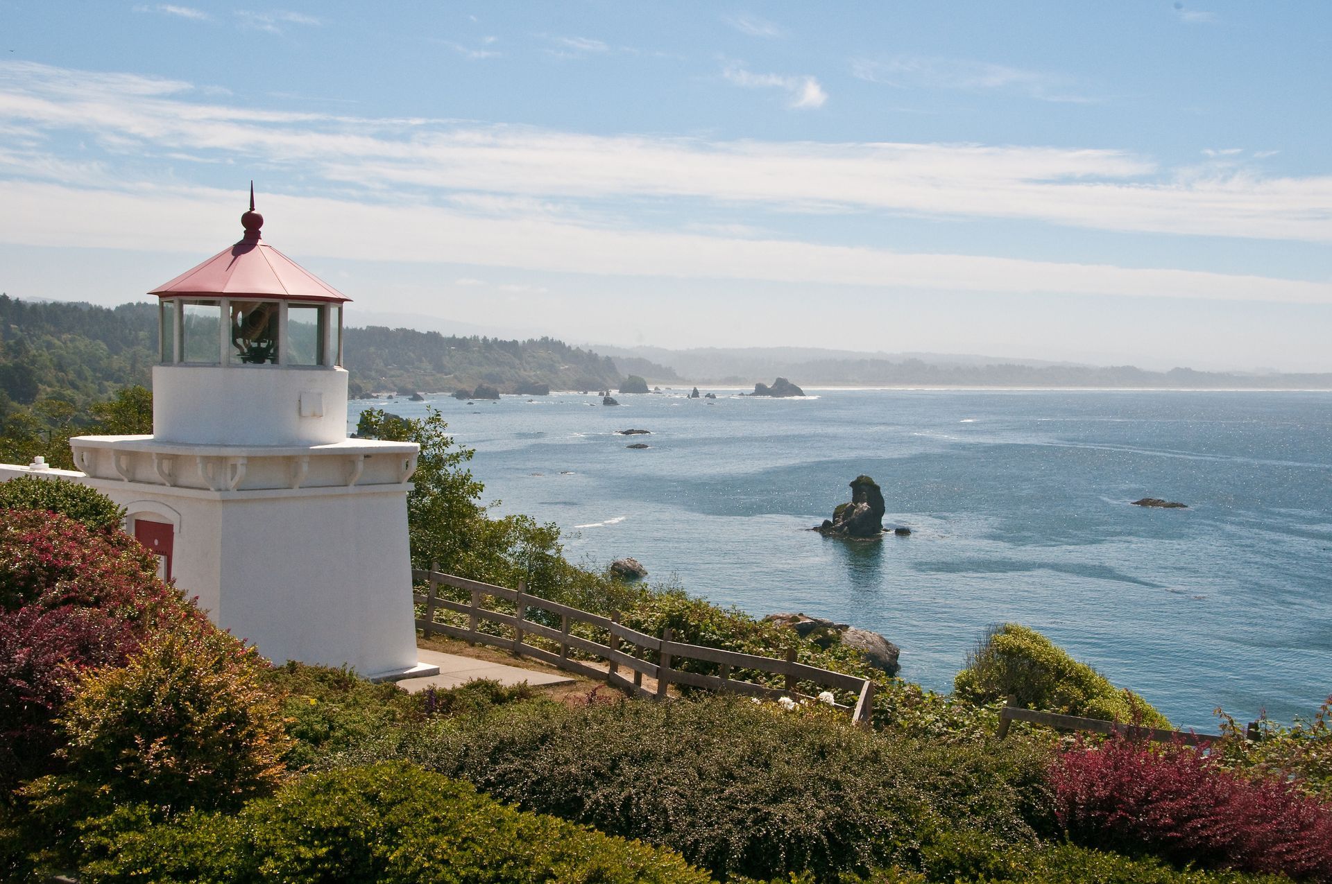 Lighthouse with red roof overlooking blue ocean and rocky coastline on a sunny day.