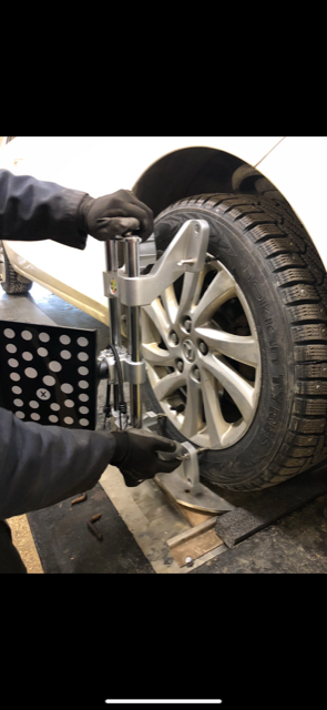 Dans un atelier de réparation automobile, un technicien ganté fixe une cible numérique d'alignement des roues sur un pneu.