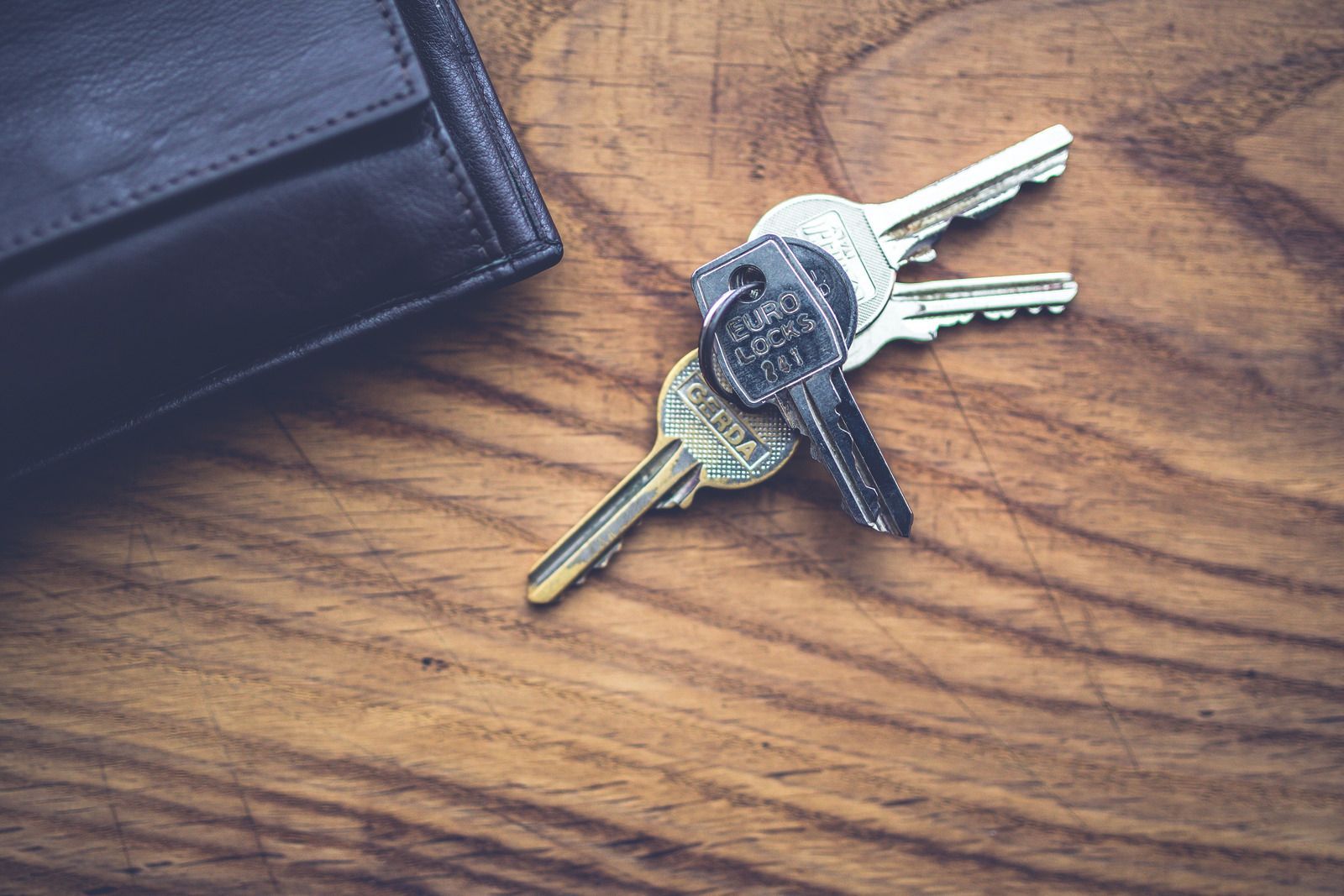 Silver keys on a keyring beside a silver lock cylinder on a wooden surface