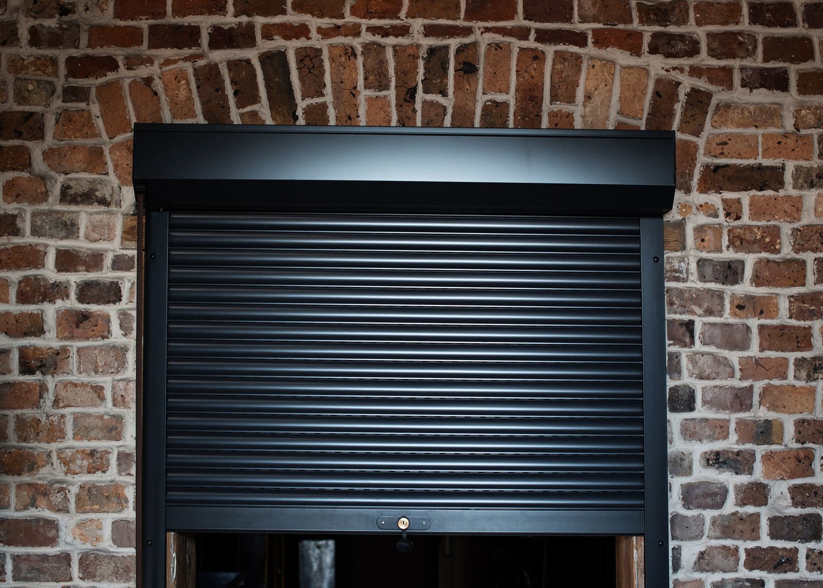 Closed dark gray metal shutter set in a brick wall opening