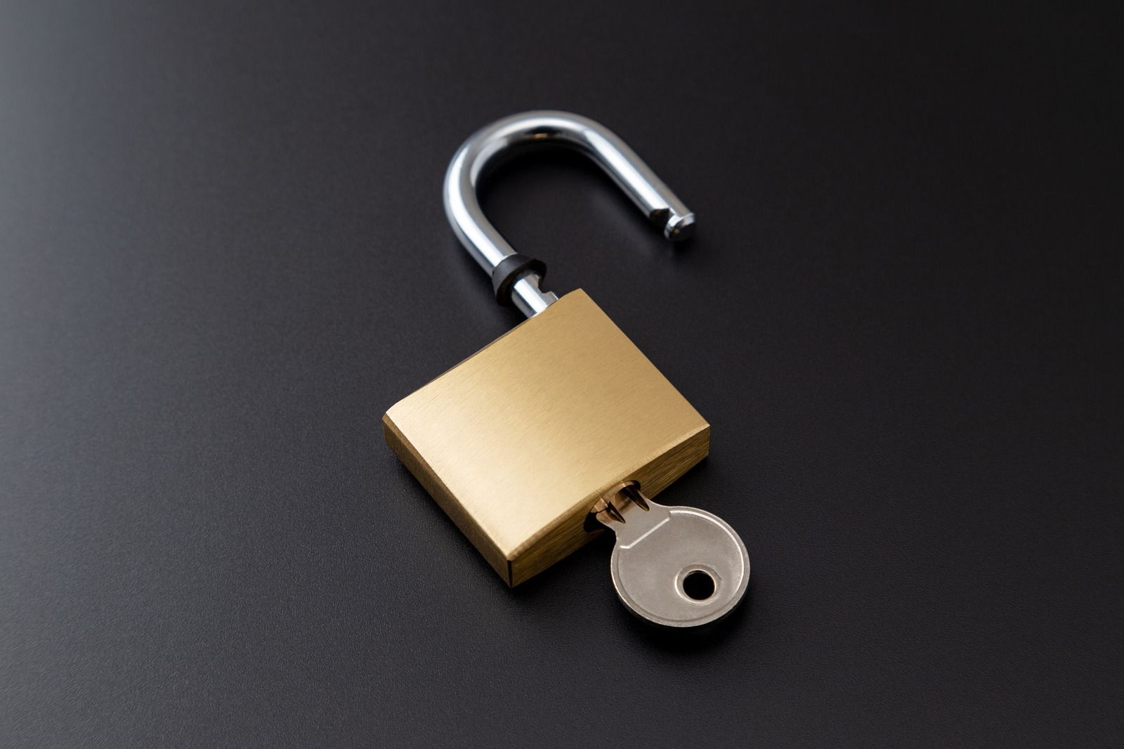 Open gold padlock with silver shackle and key on a dark background