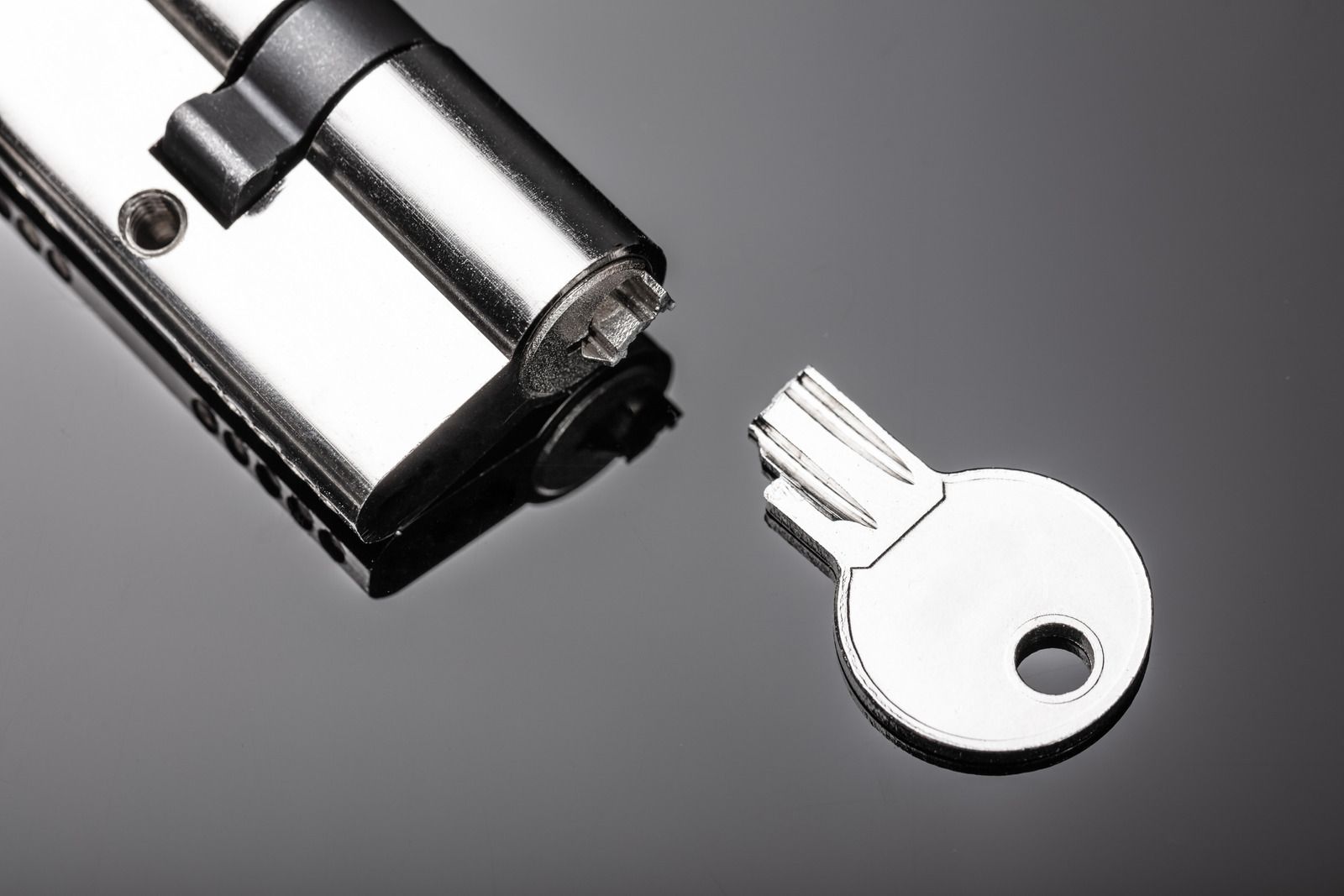 Silver key next to a chrome door lock on a gray background