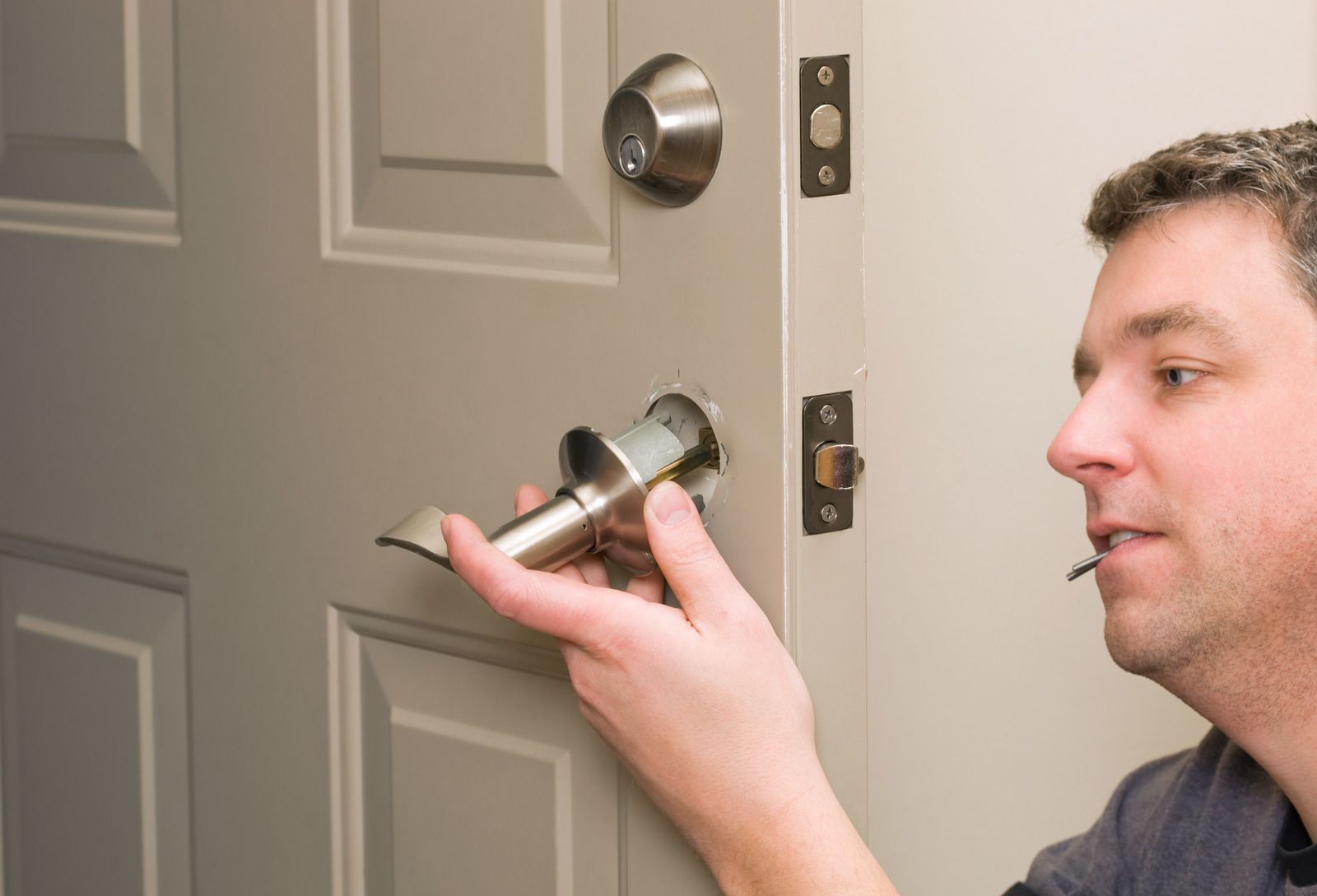 Man installing a silver door lock on a gray front door