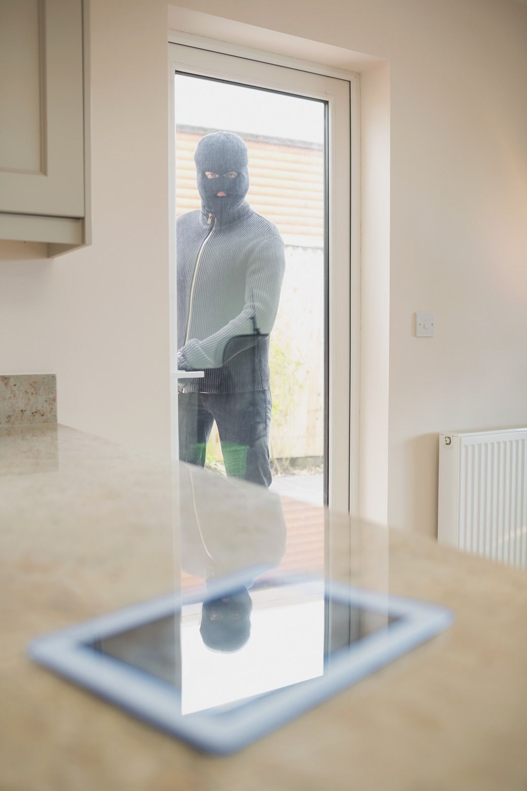 Person standing at a glass door, seen through a kitchen window beside a counter and radiator.