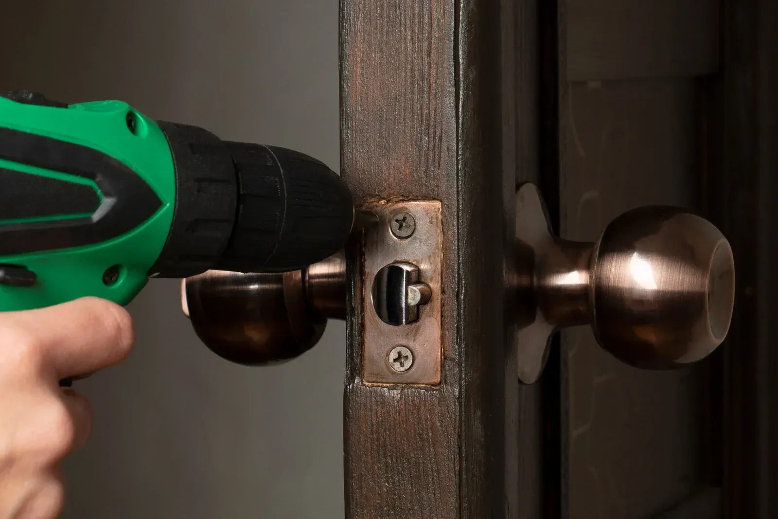 Green drill removing a bronze door handle from a wooden door