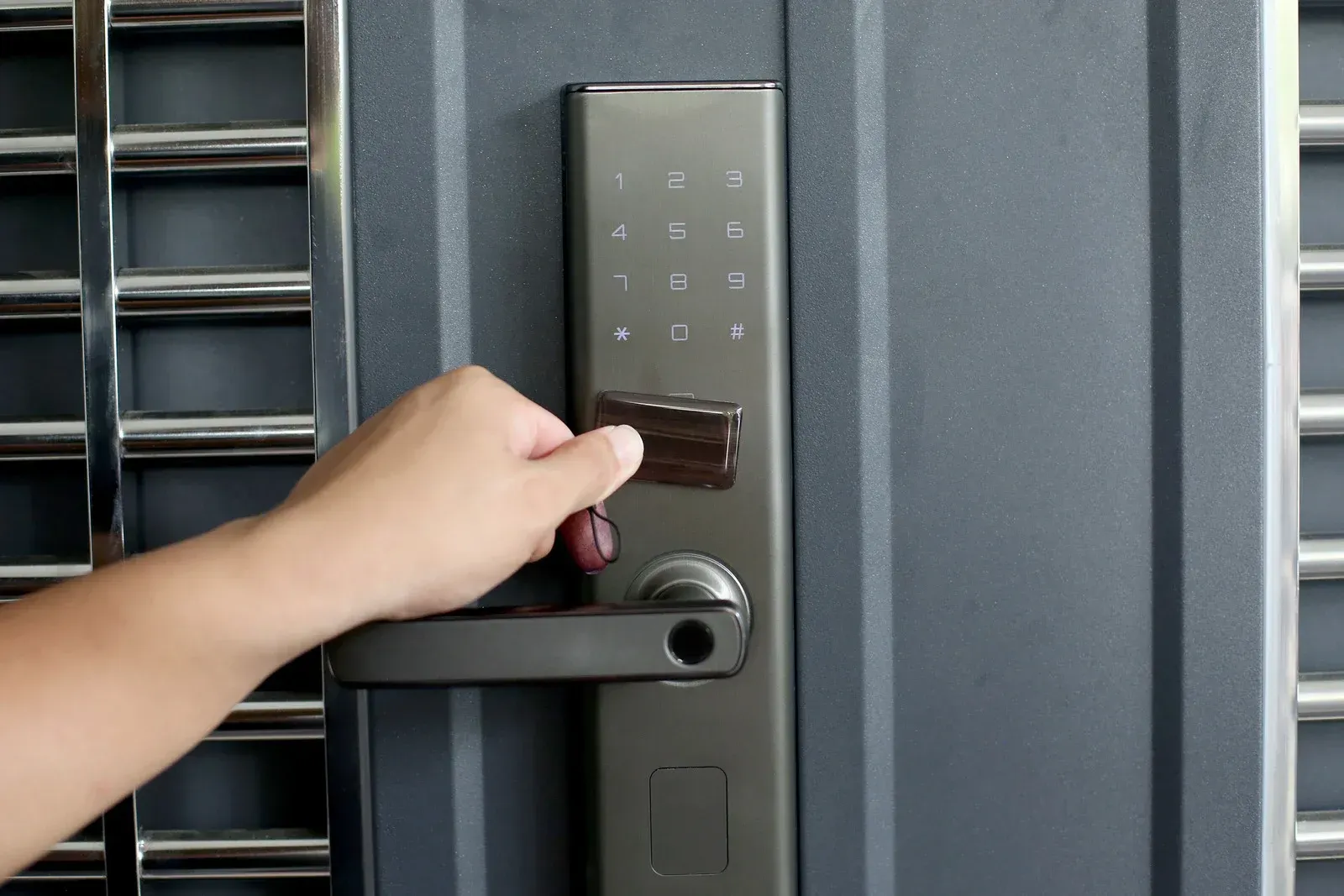 Hand unlocking a gray keypad door with a card reader and horizontal handle