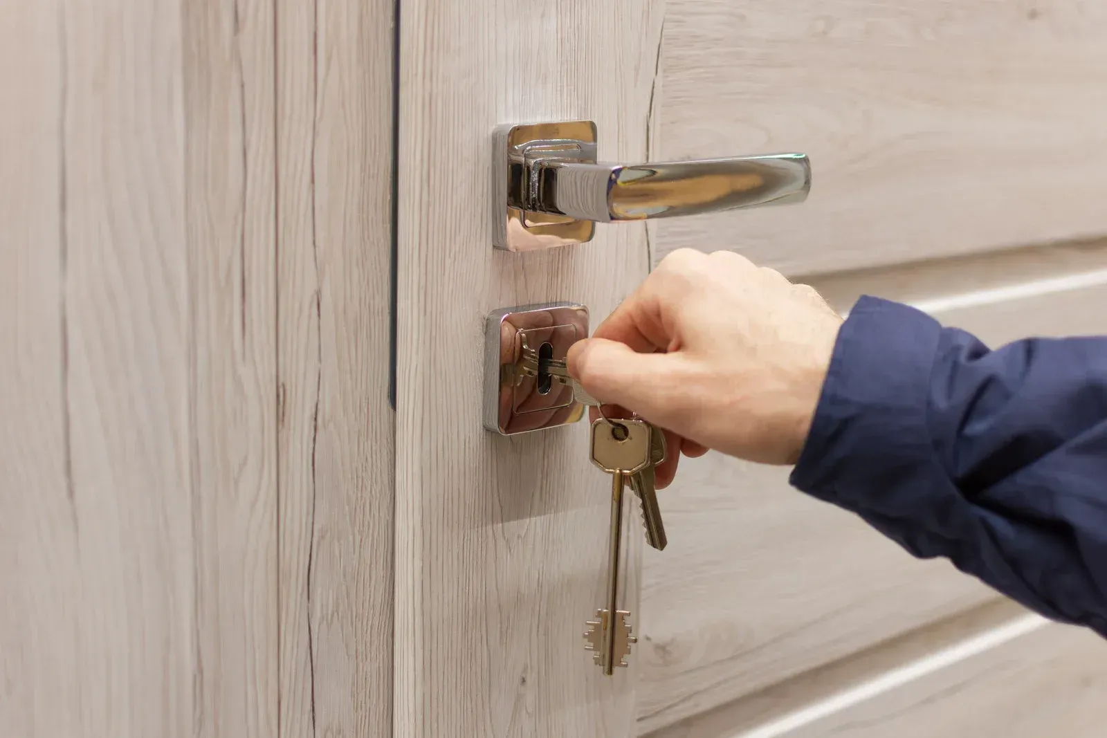 Hand unlocking a beige door with a key in the lock