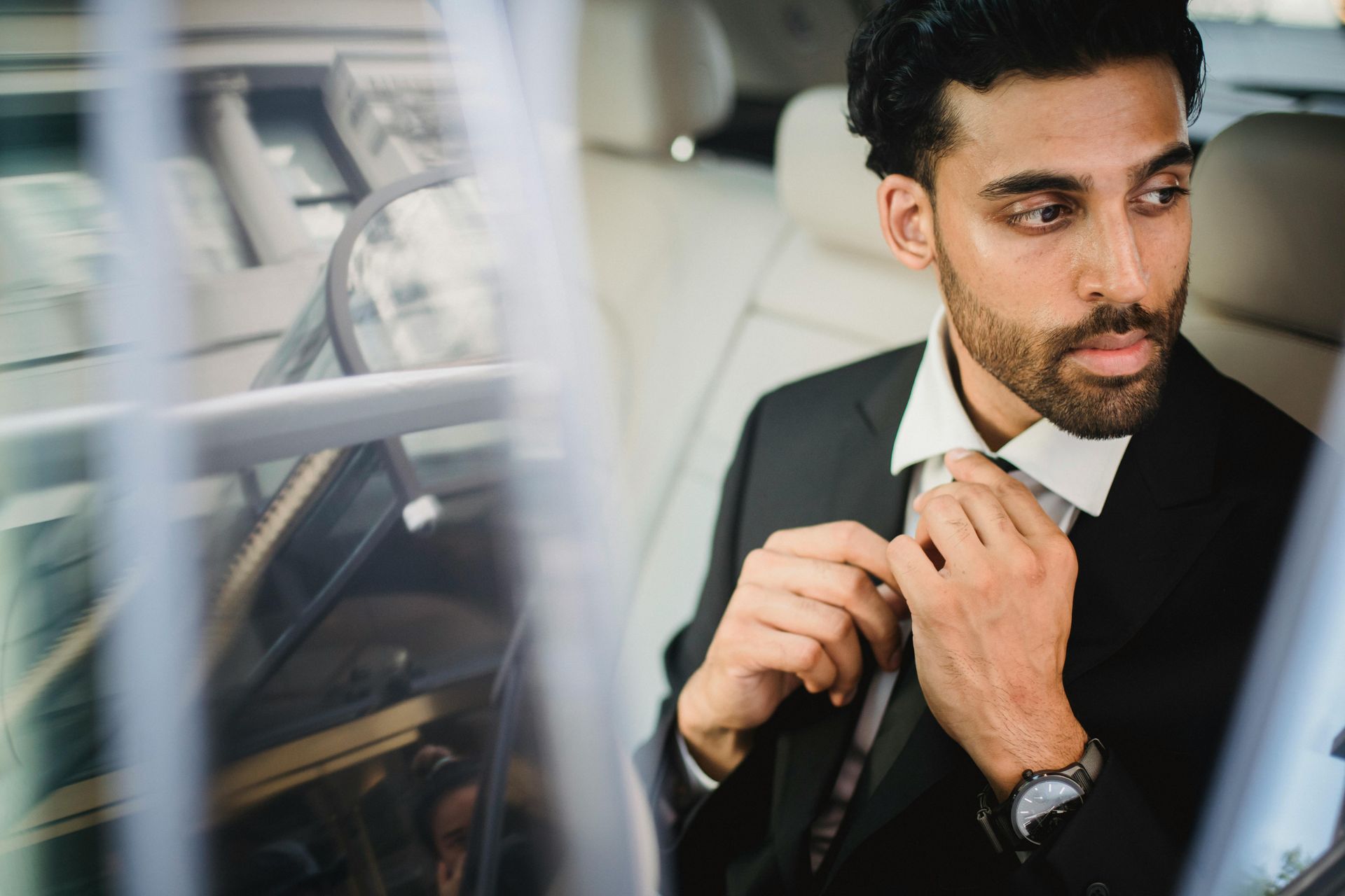 A man in a suit is tying his tie in the back seat of a car.