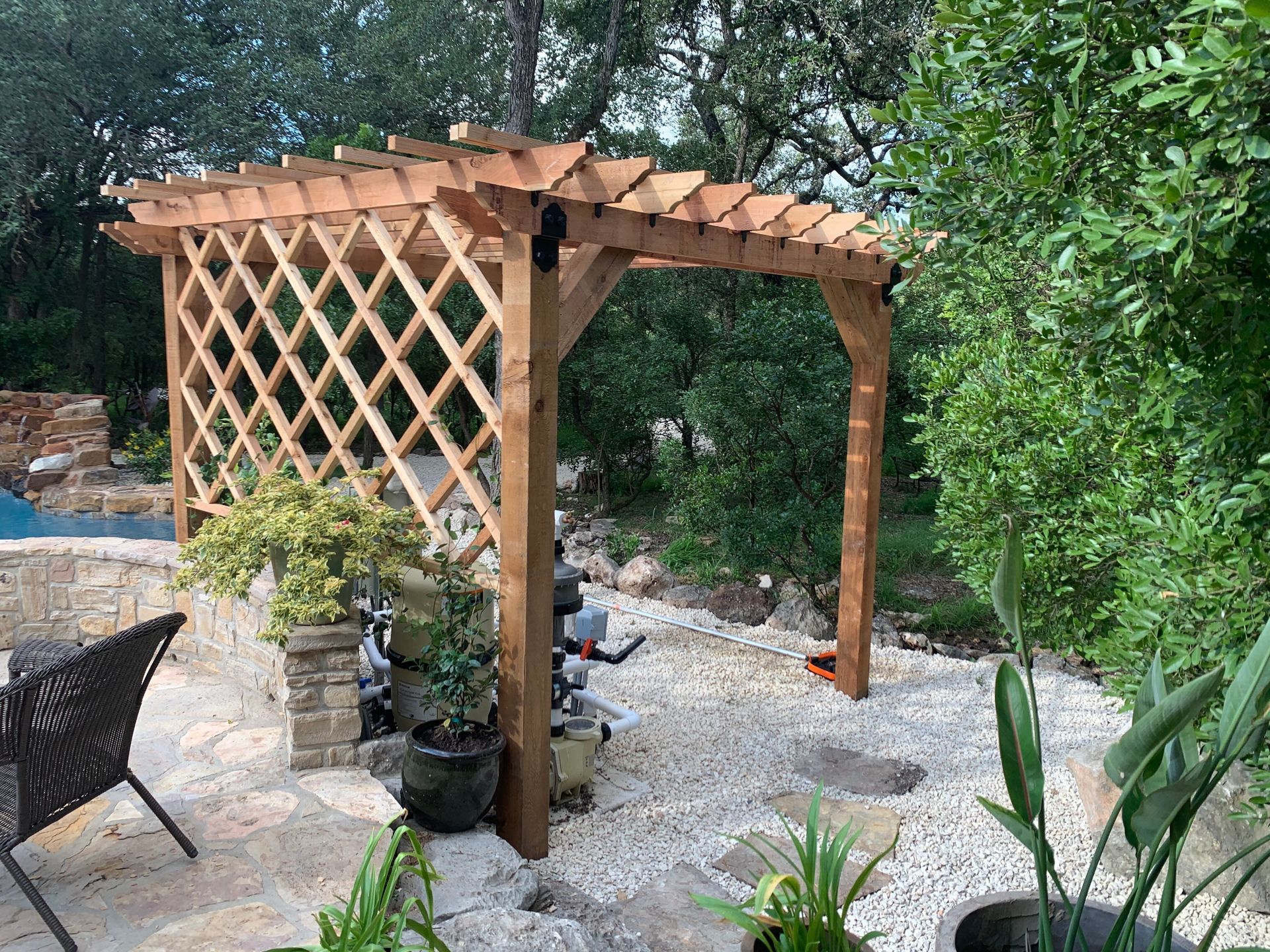 Wooden pergola with latticework and gravel path in a garden setting.