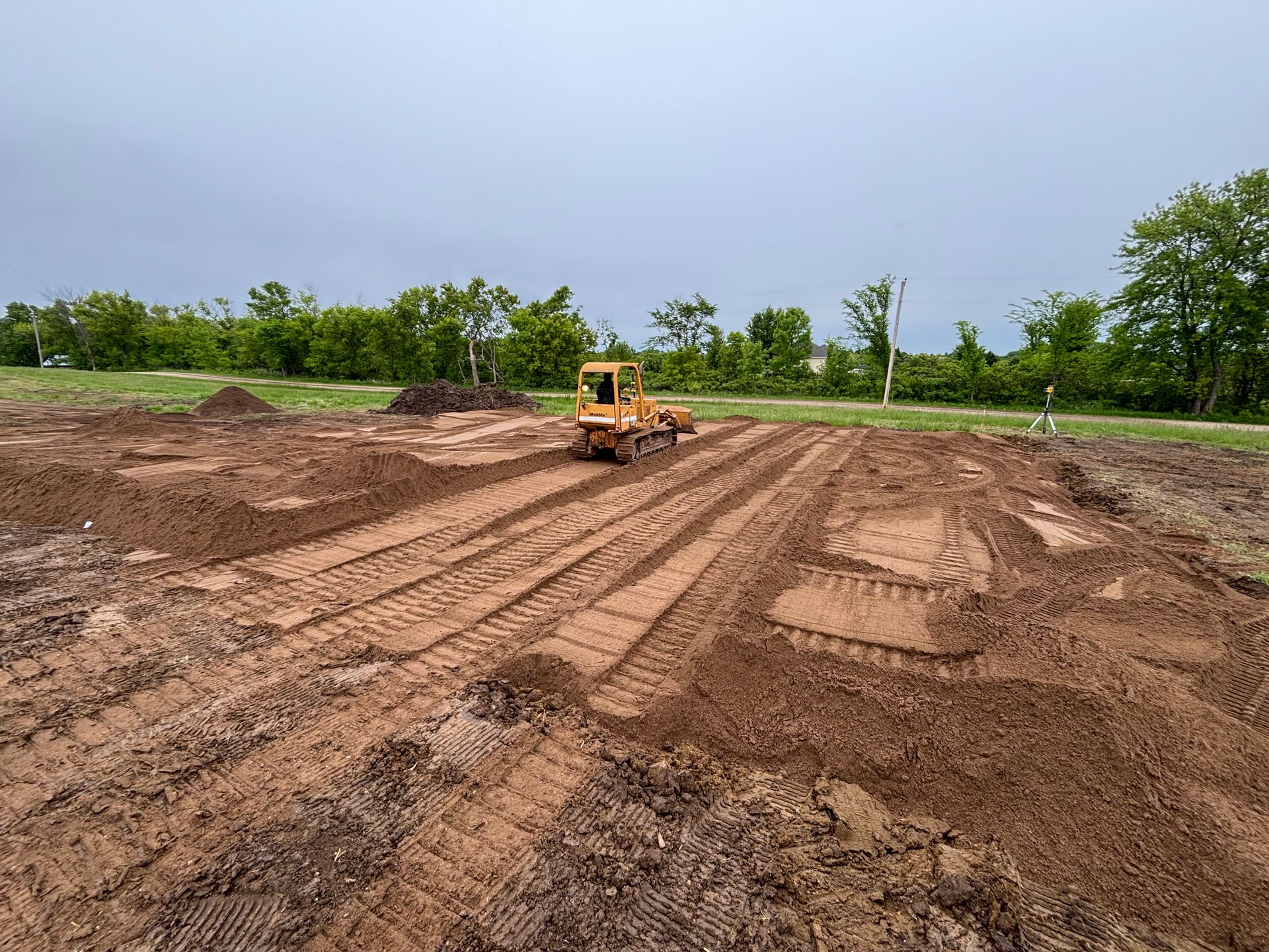 A yellow bulldozer moves earth in a large, muddy field under a cloudy sky.