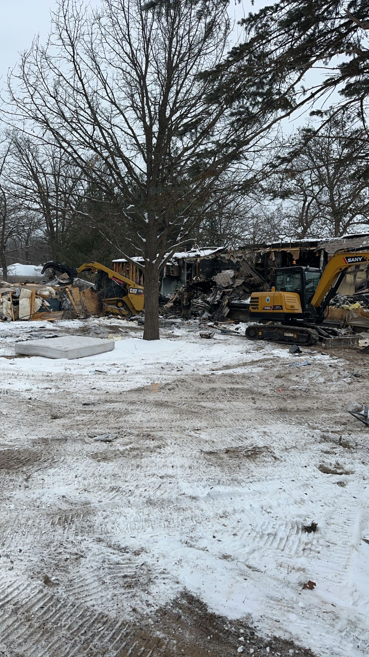 Yellow excavators demolish a building in a snowy, wooded area.