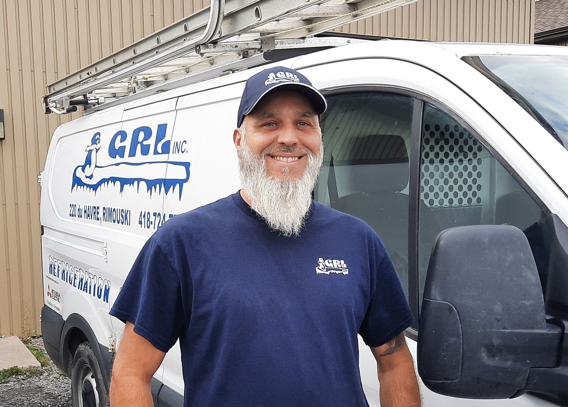 Un homme barbu, portant une chemise bleue et un chapeau, se tient près d'une camionnette blanche avec le logo « CRL Inc ».