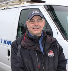 Un homme en casquette et veste, souriant, se tient devant une camionnette blanche sur laquelle on peut lire « Inspection » sur le côté.