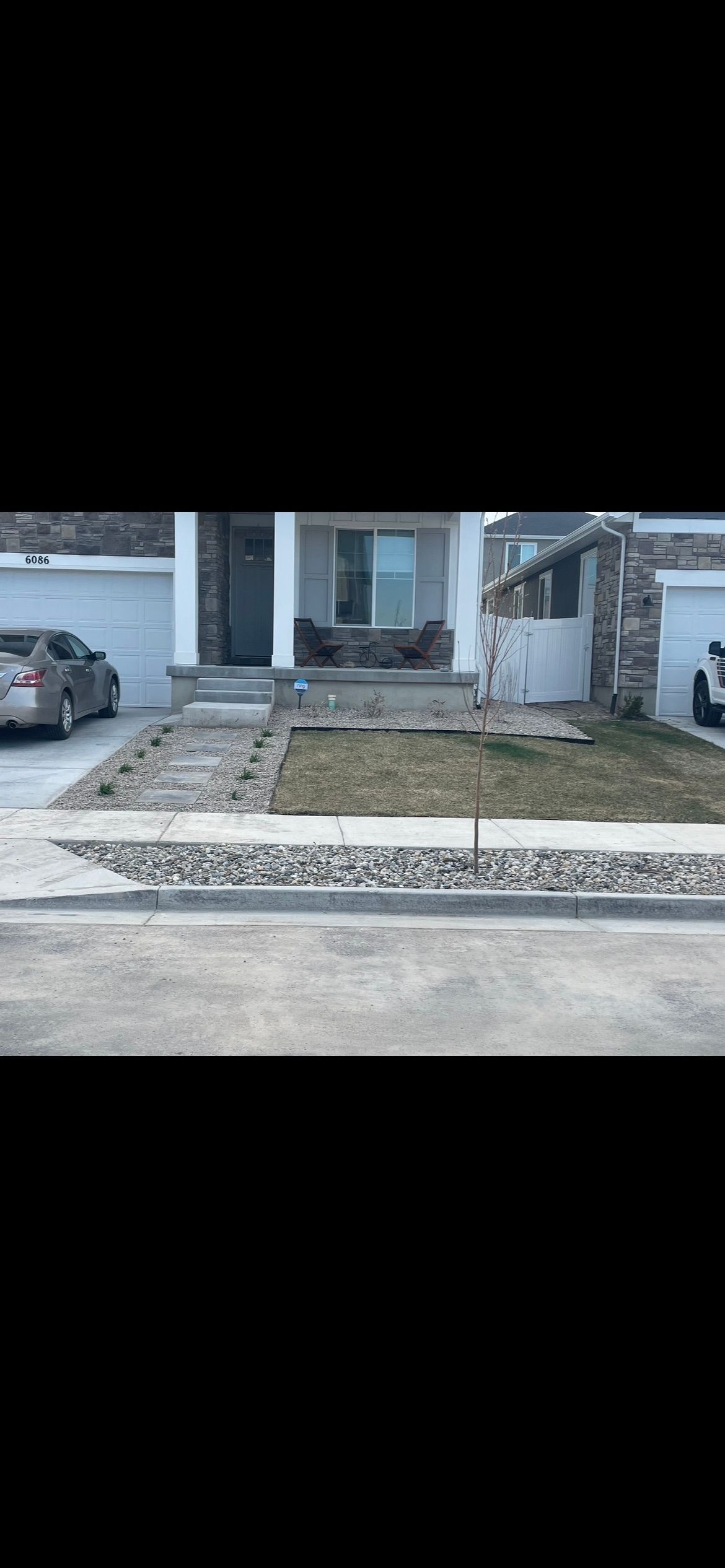 Front yard with a concrete walkway, patchy grass, a parked car, and a house entrance under construction