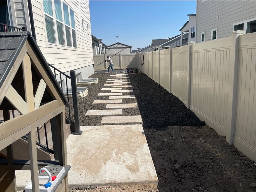 Narrow backyard walkway with concrete stepping stones, white fence, and dark mulch between houses
