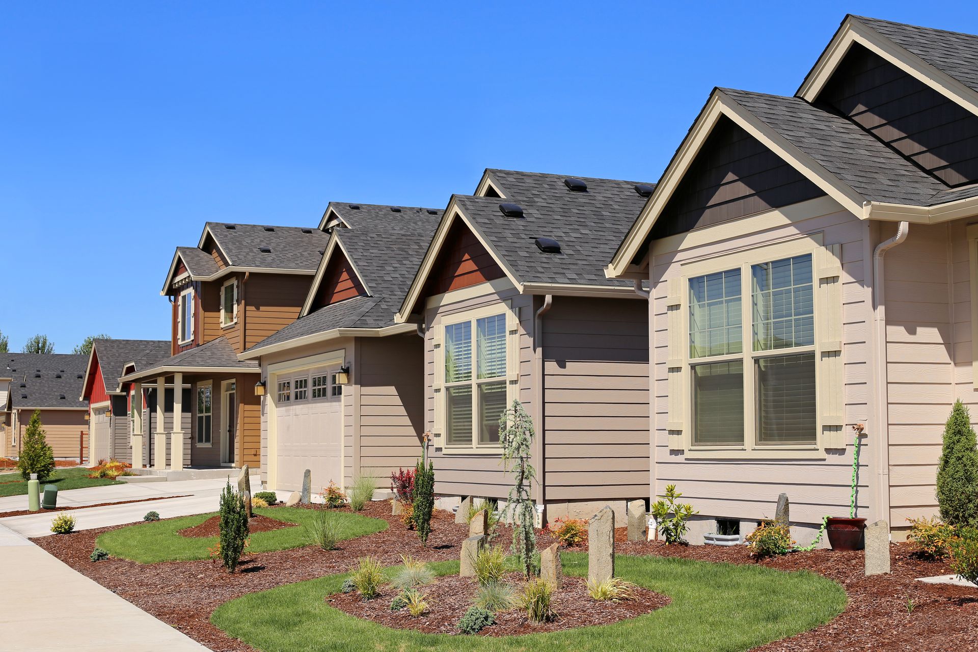 A row of modern, beige-sided suburban houses with gray roofs under a clear blue sky.