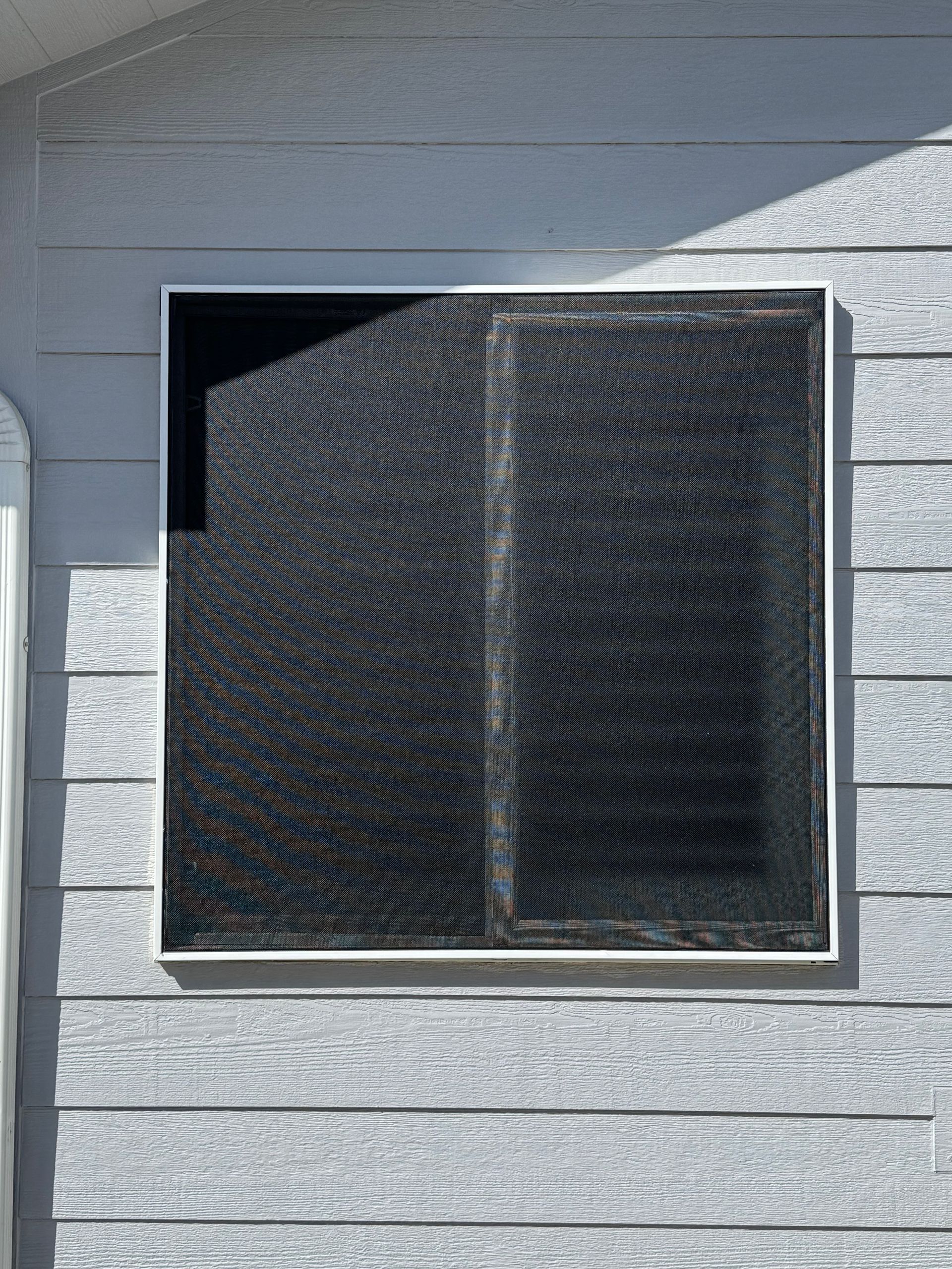A window with a screen on it is on the side of a house.