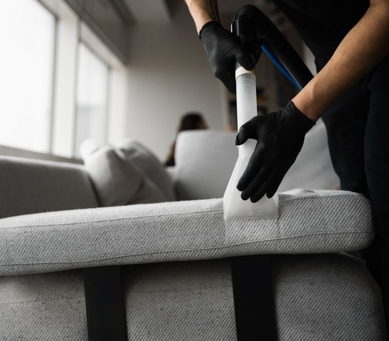 A person is cleaning a couch with a vacuum cleaner.