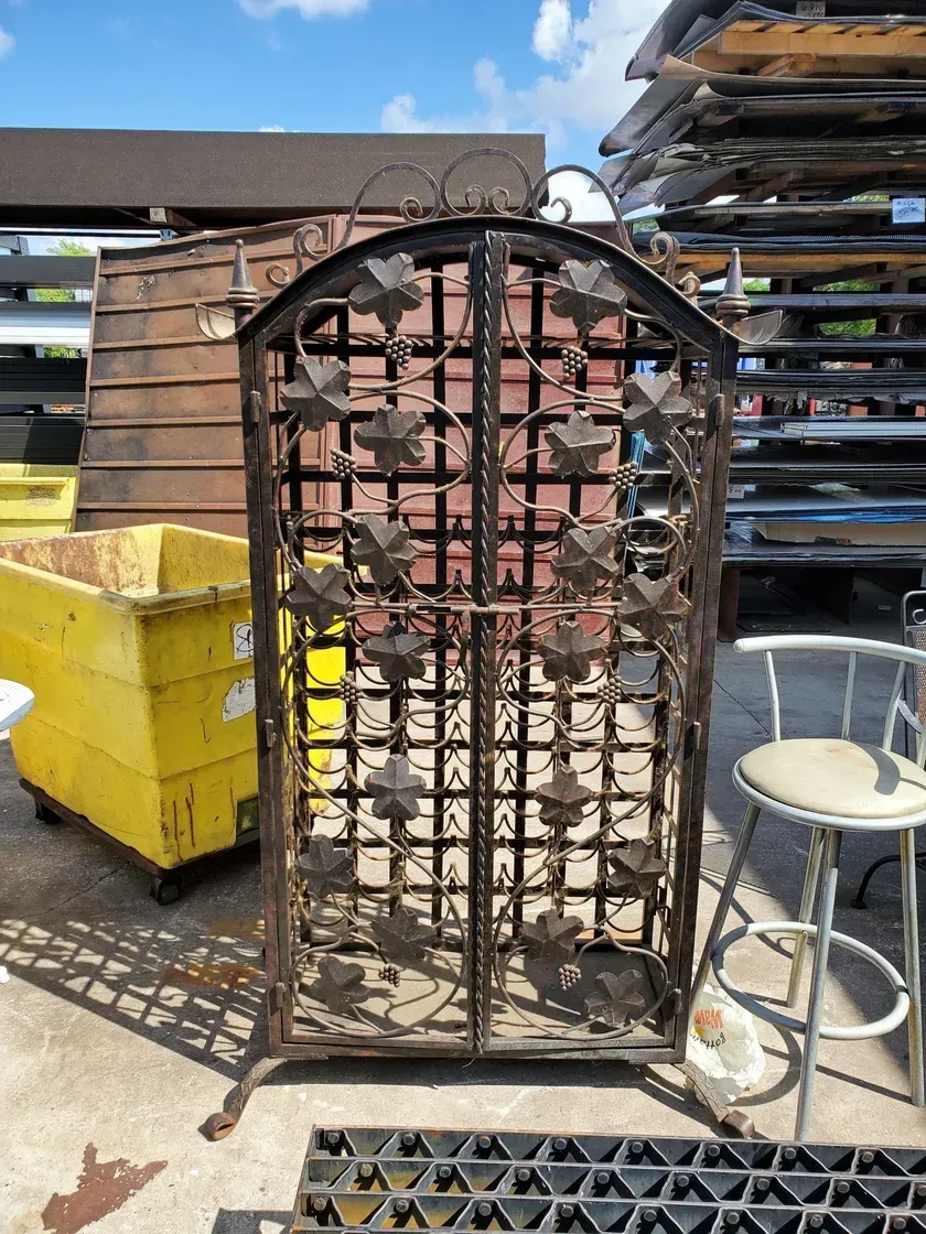 A wrought iron gate with leaves on it is sitting on the ground in a yard.