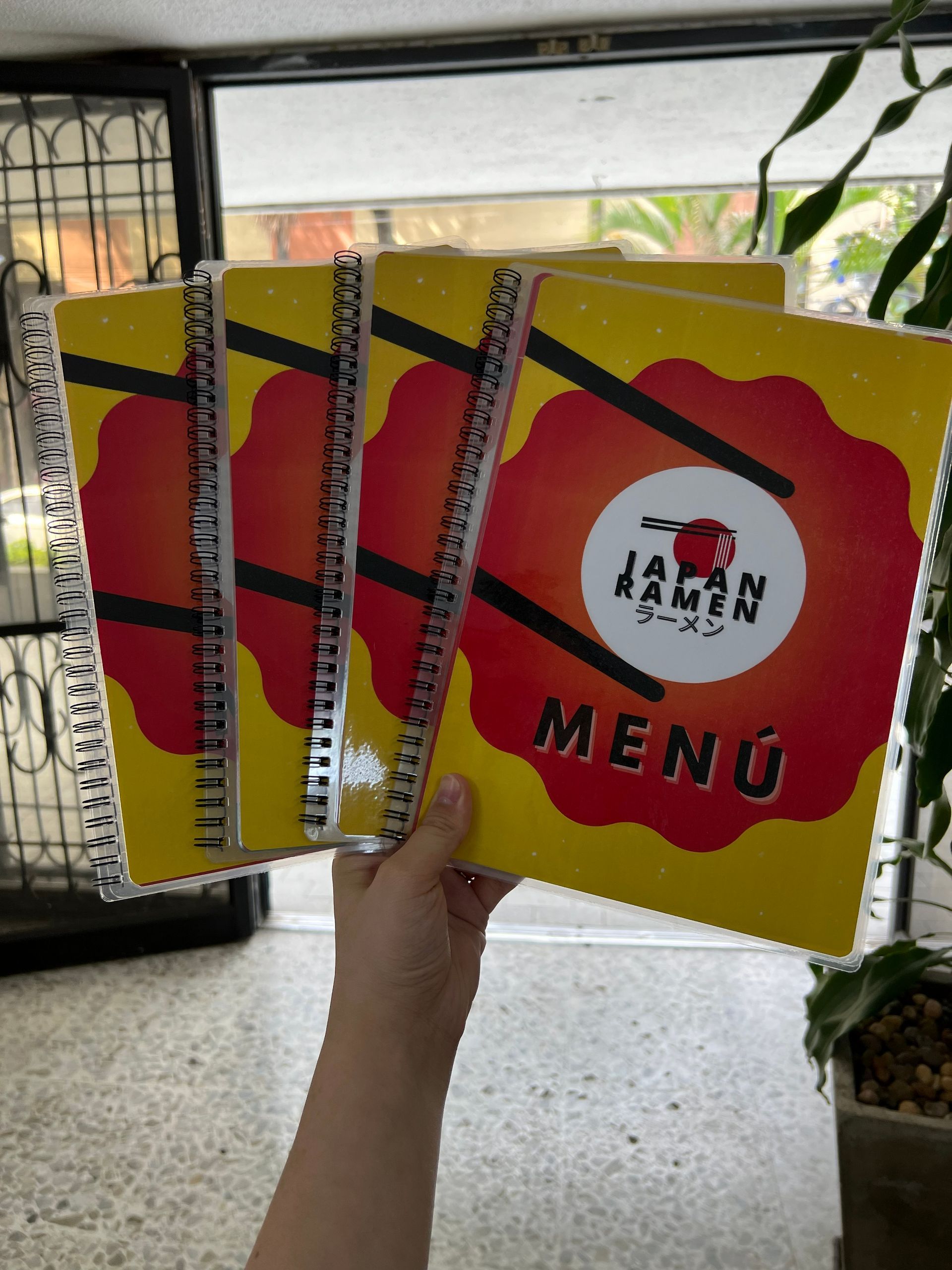Una mano sostiene tres coloridos menús de restaurante con portadas rojas y amarillas en el interior.