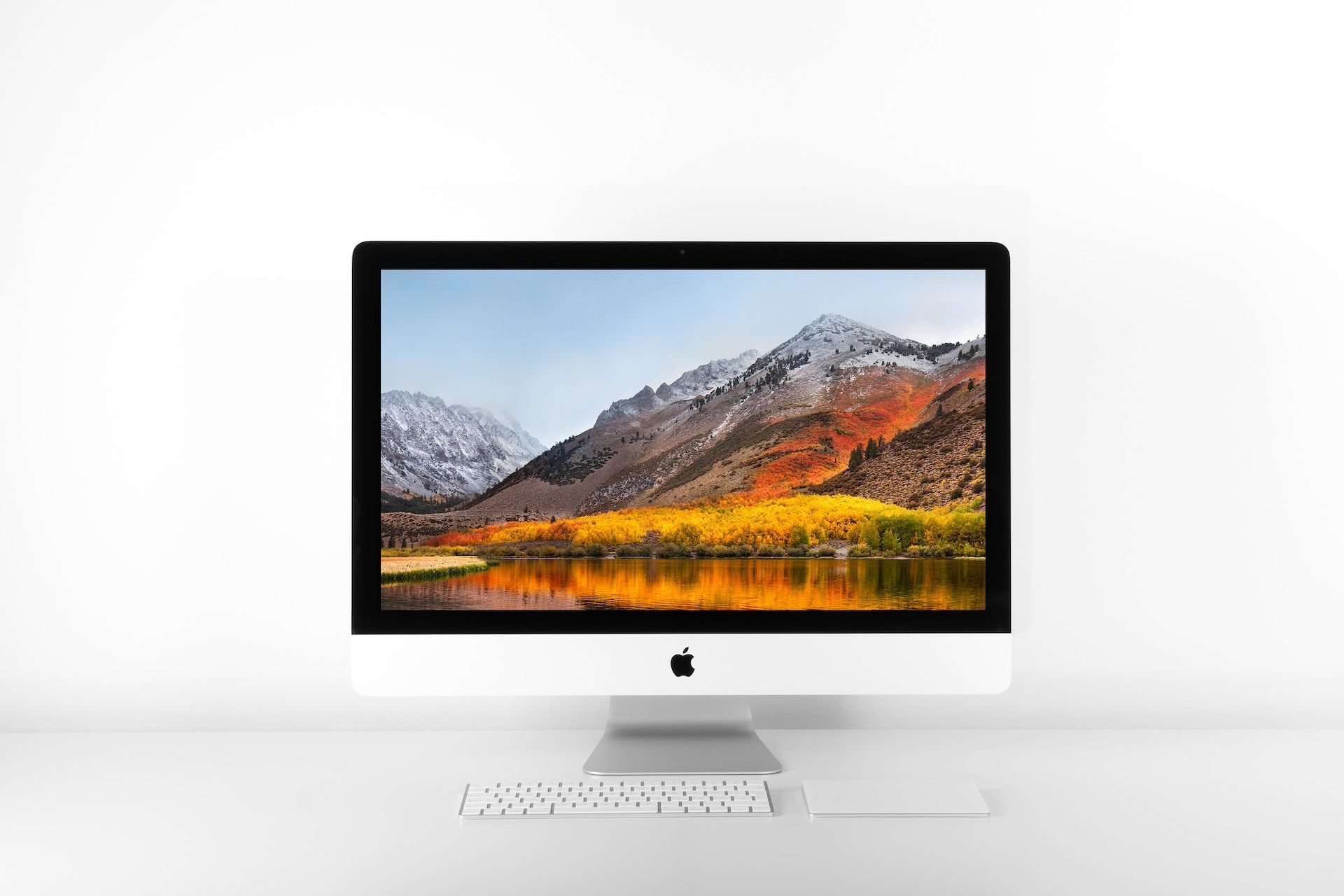 apple imac desktop that's on with screen showing mountain with snow background & water
