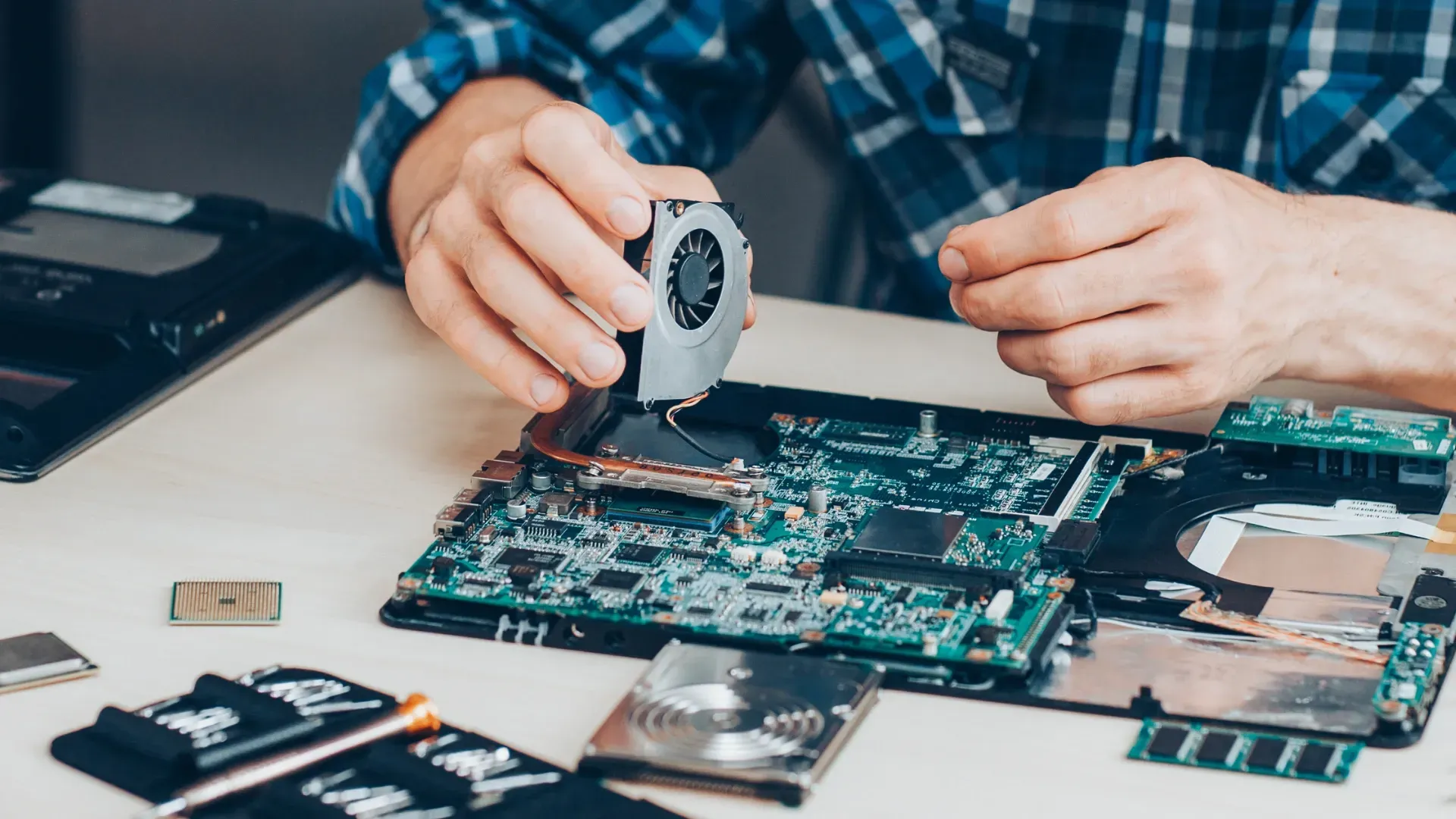 technician installing laptop fan during laptop repair with screw drive, cpu and other components taken from laptop on work desk