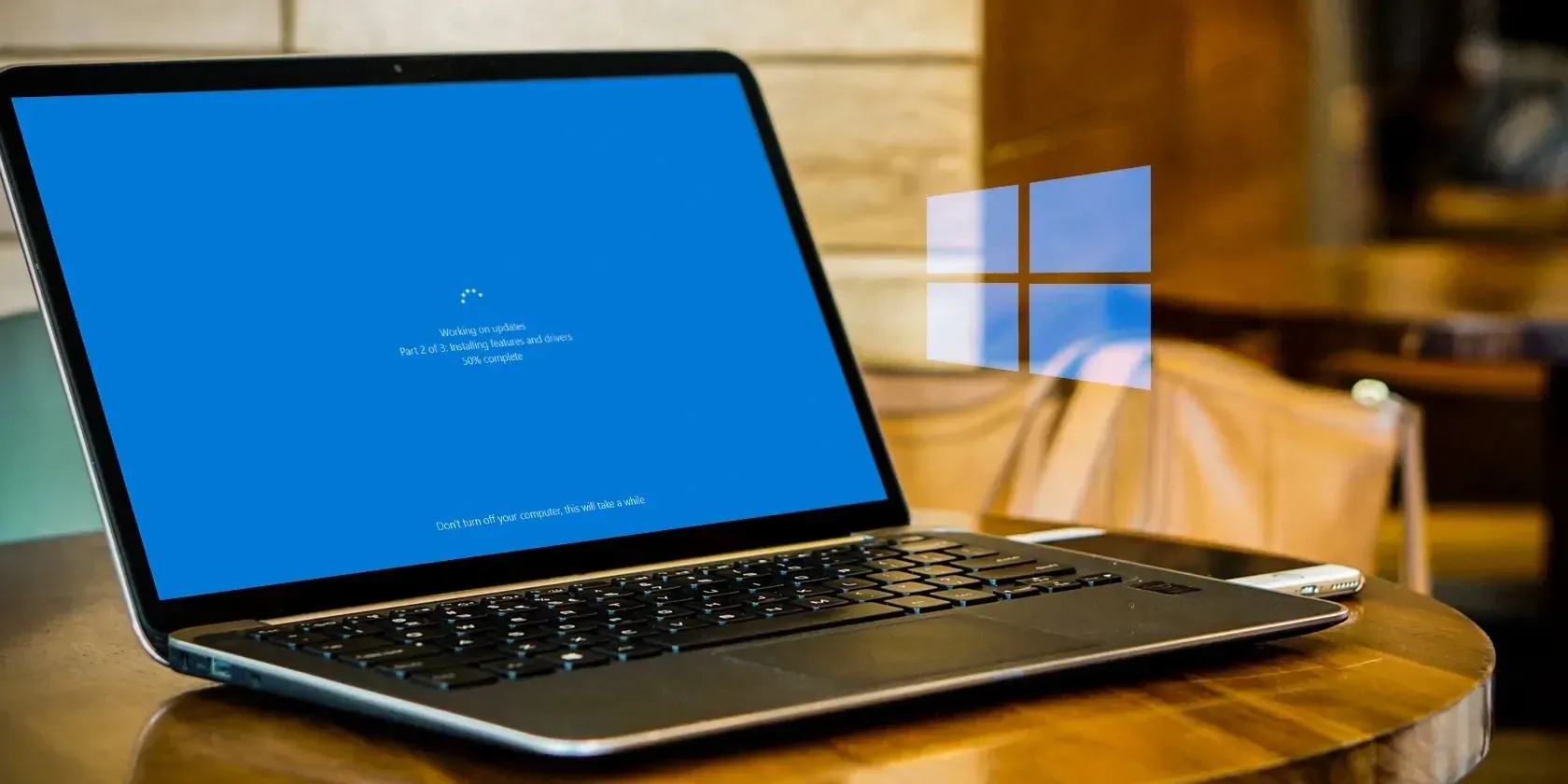 laptop pc with screen open and updating on a table with phone next to it