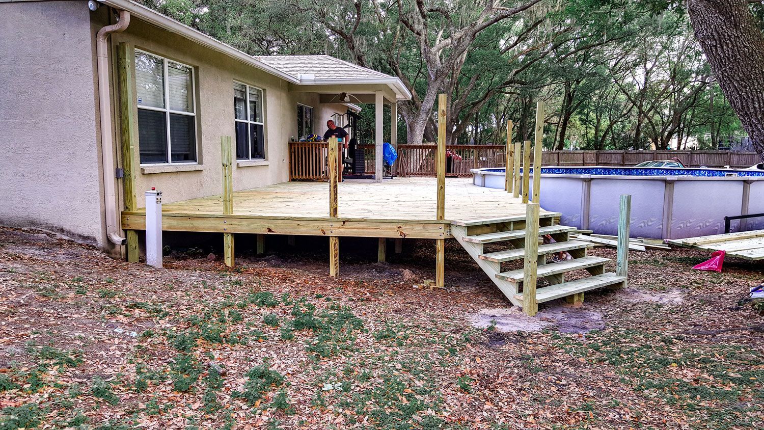Newly built wooden deck with stairs and railing, leading to a pool in a backyard.