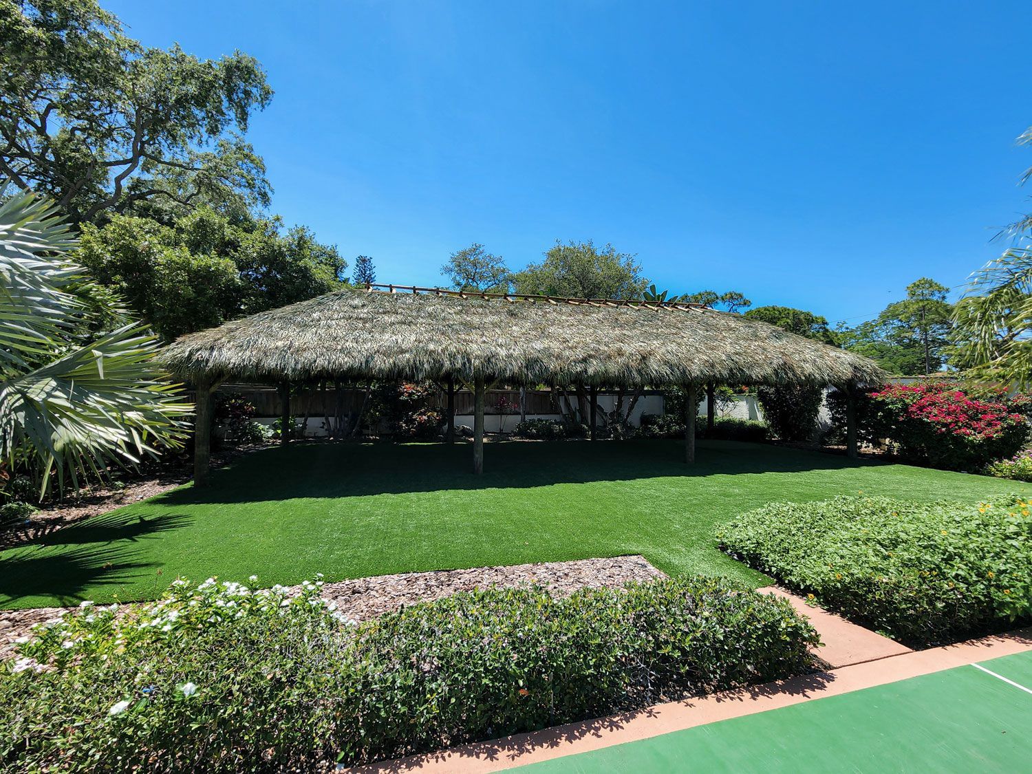 Thatched roof structure over green grass and landscaping, under blue sky.