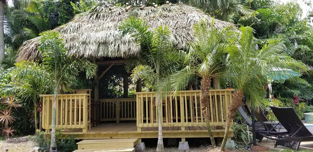 Tropical-style gazebo with thatched roof, surrounded by palm trees and greenery; poolside. Tropical-style gazebo with thatched roof, surrounded by palm trees and greenery; poolside.
