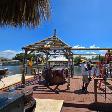 Wooden dock with tiki hut and workers on a sunny day.