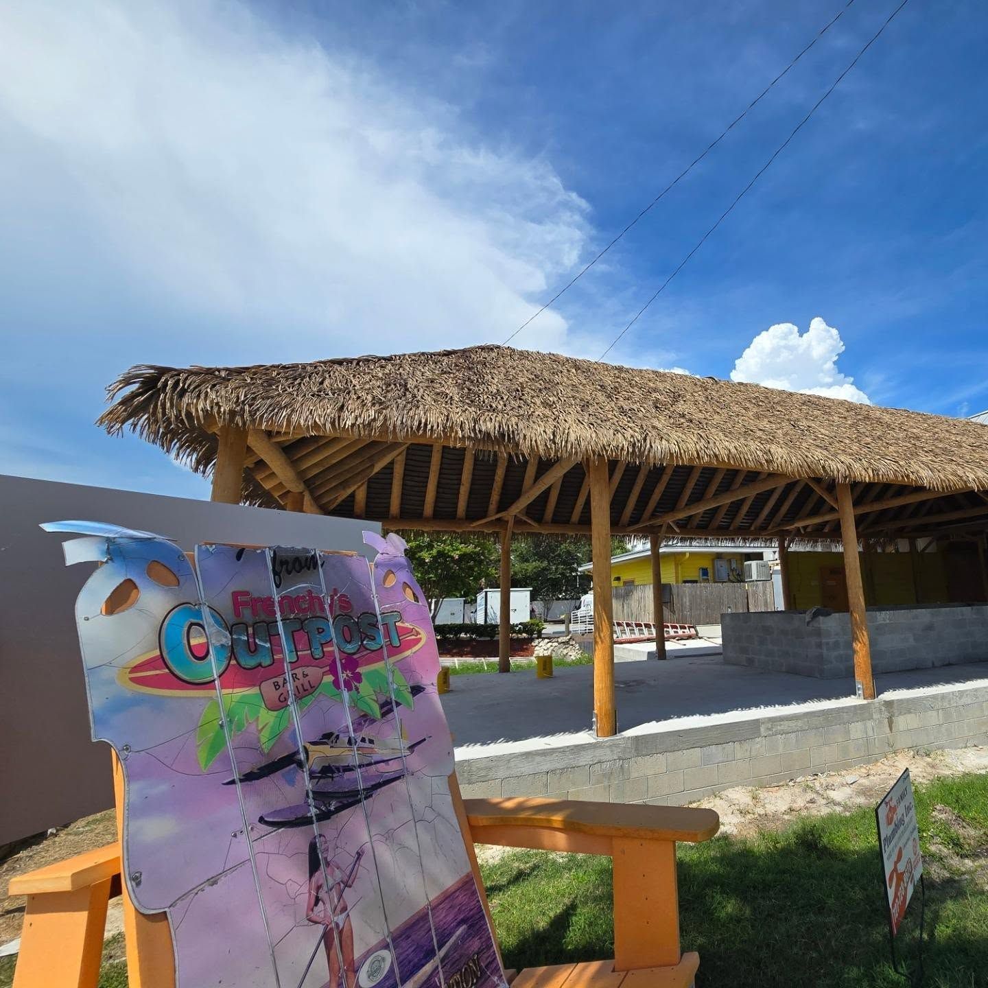 A thatched roof structure with a colorful sign in the foreground under a blue sky. A thatched roof structure with a colorful sign in the foreground under a blue sky.