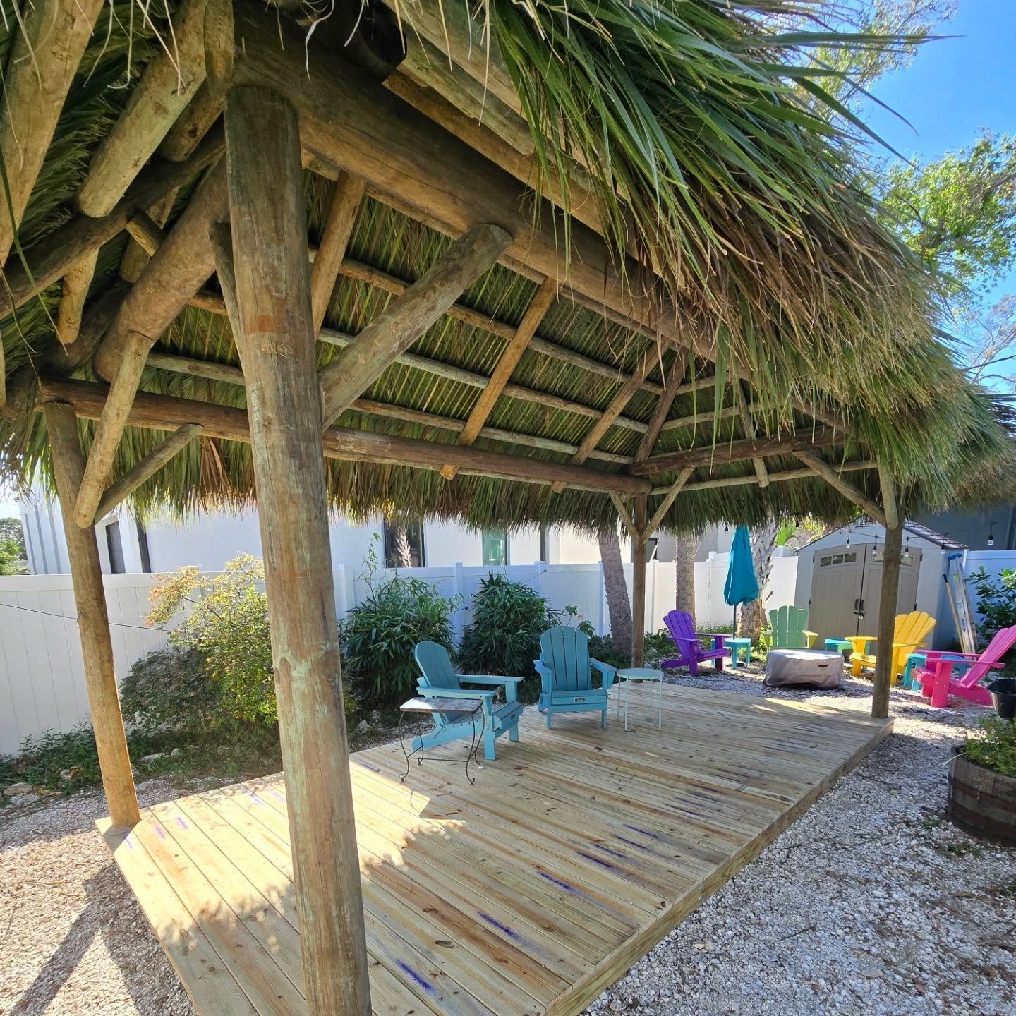 Wooden tiki hut over a deck with colorful Adirondack chairs; bright outdoor setting. Wooden tiki hut over a deck with colorful Adirondack chairs; bright outdoor setting.
