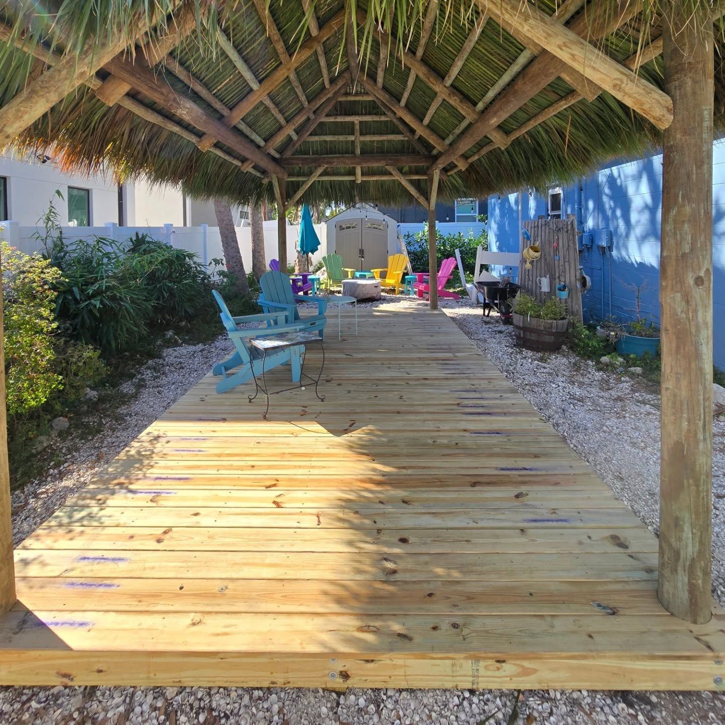 Wooden walkway under thatched roof, leading to colorful chairs and yard. Wooden walkway under thatched roof, leading to colorful chairs and yard.