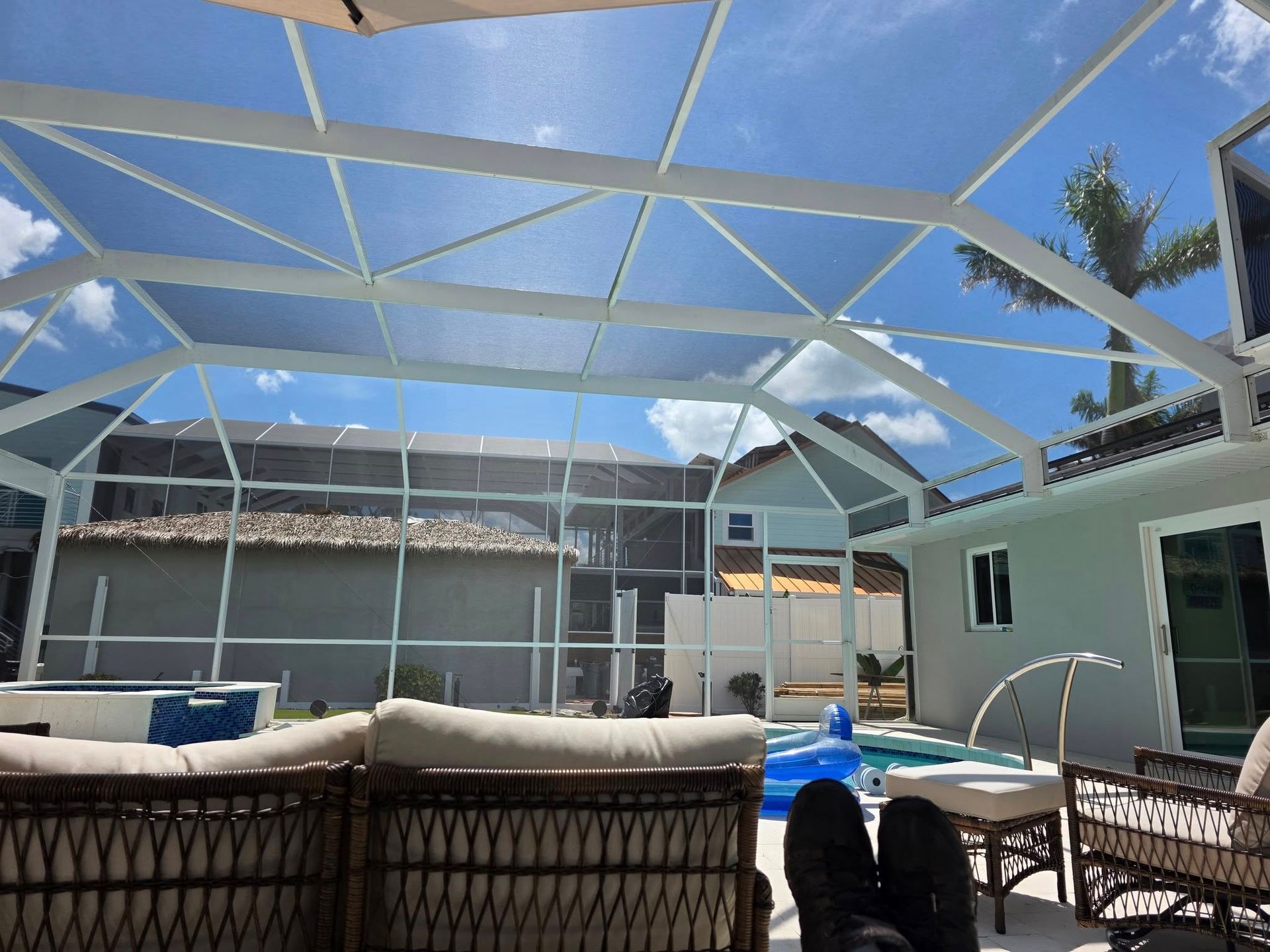 Pool patio with white screened enclosure, wicker furniture, and blue sky. Pool patio with white screened enclosure, wicker furniture, and blue sky.