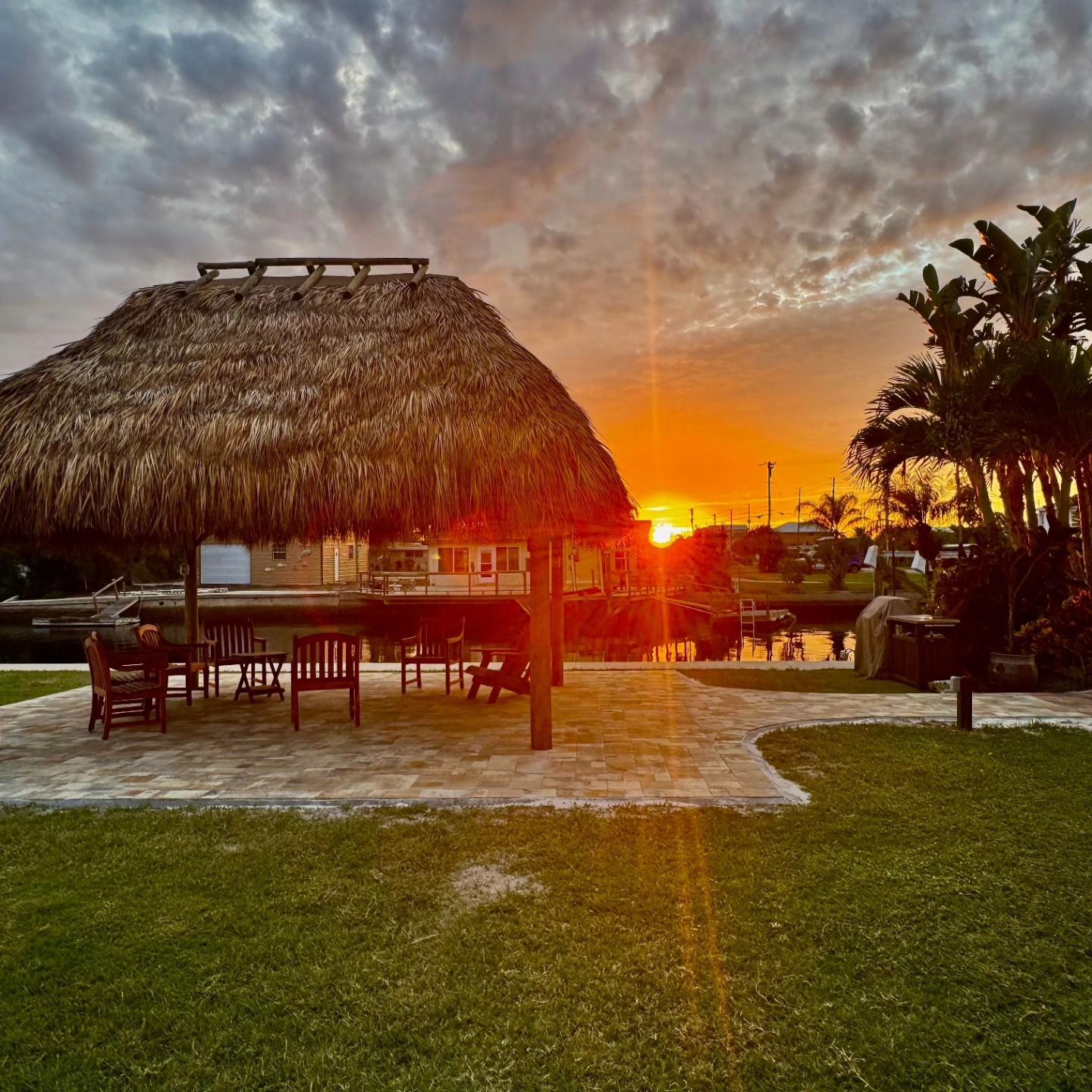 Sunset over a thatched-roof cabana by a waterway with a grassy lawn. Sunset over a thatched-roof cabana by a waterway with a grassy lawn.