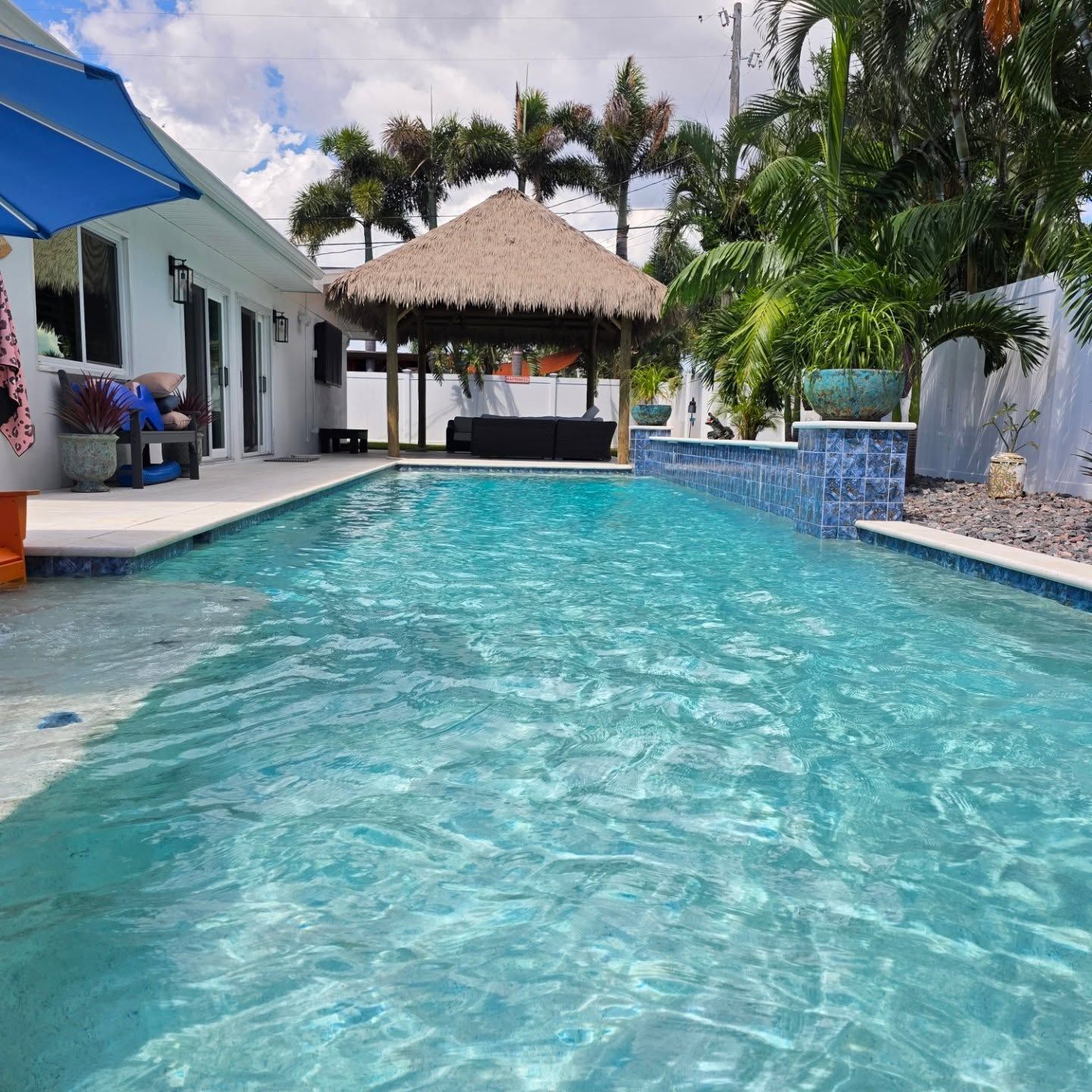 Pool in tropical setting; white house, thatched roof cabana, palm trees, blue water. Pool in tropical setting; white house, thatched roof cabana, palm trees, blue water.