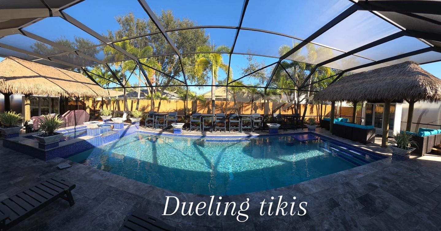 A backyard pool with two tiki huts, surrounded by a screened enclosure under a clear blue sky. A backyard pool with two tiki huts, surrounded by a screened enclosure under a clear blue sky.
