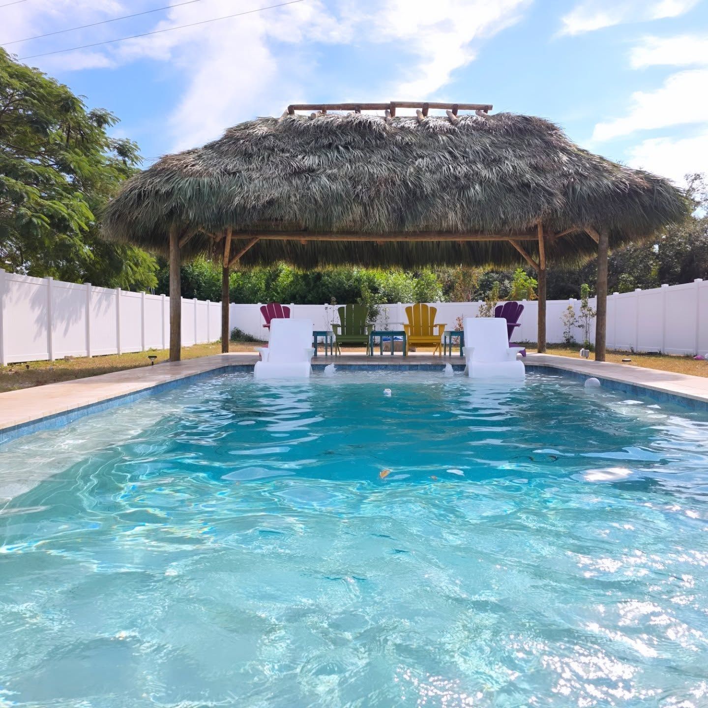 Swimming pool with thatch roof shelter, white chairs, blue water, sunny day. Swimming pool with thatch roof shelter, white chairs, blue water, sunny day.