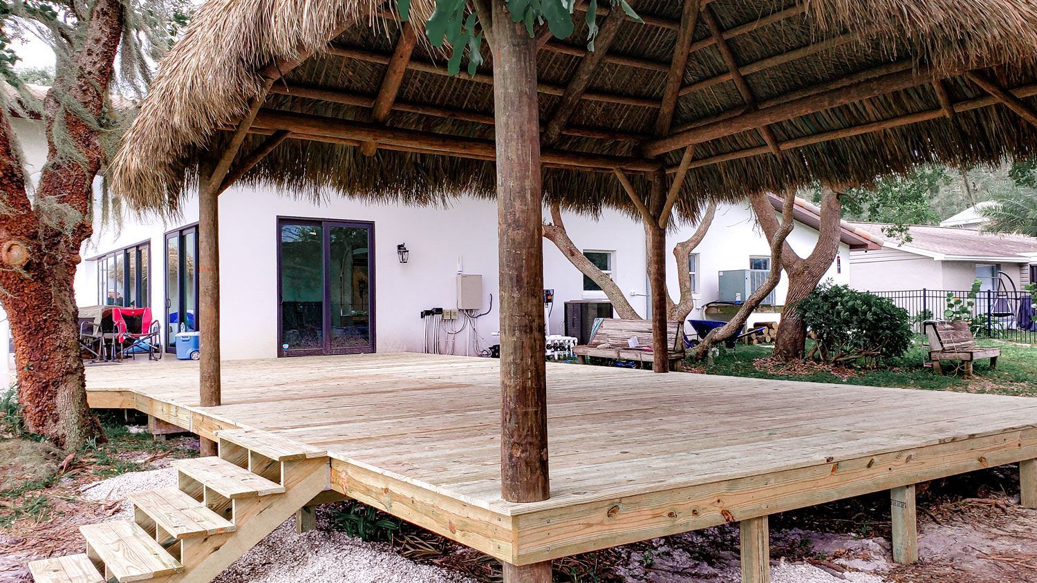 Wooden deck with a thatched-roof gazebo. A white house is in the background.