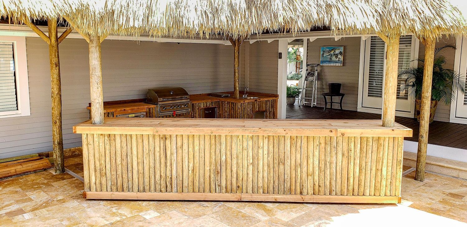 A tiki-style bar with a thatched roof, surrounded by sand and a light-colored building. A tiki-style bar with a thatched roof, surrounded by sand and a light-colored building.