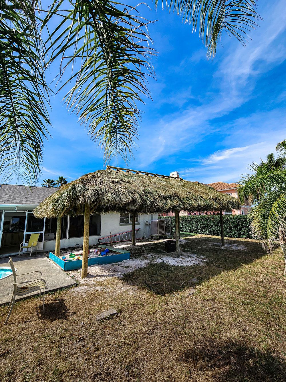 Thatched roof shade structure in a yard with blue sky.